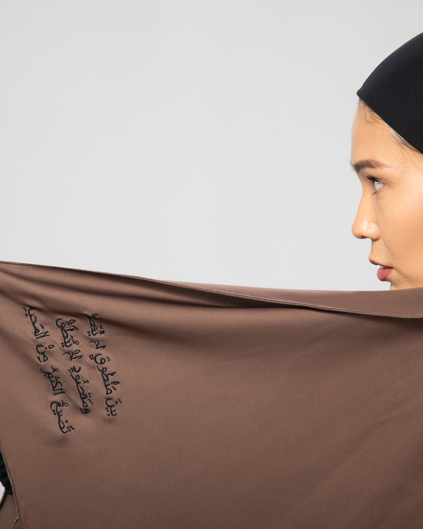 Close-up of the brown Flow Abaya’s front panel, featuring Arabic calligraphy embroidery that reads: “Between what was said and not meant and what was meant but not said, most love is lost.” KSA UAE Qatar