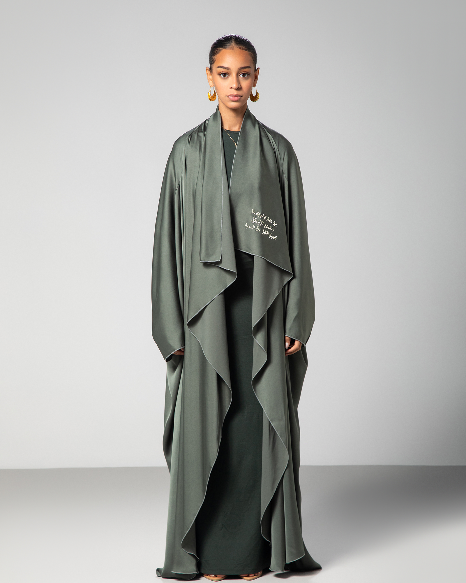 A woman wearing a green flowing abaya with cascading layers and embroidery on the front.UAE Qatar KSA