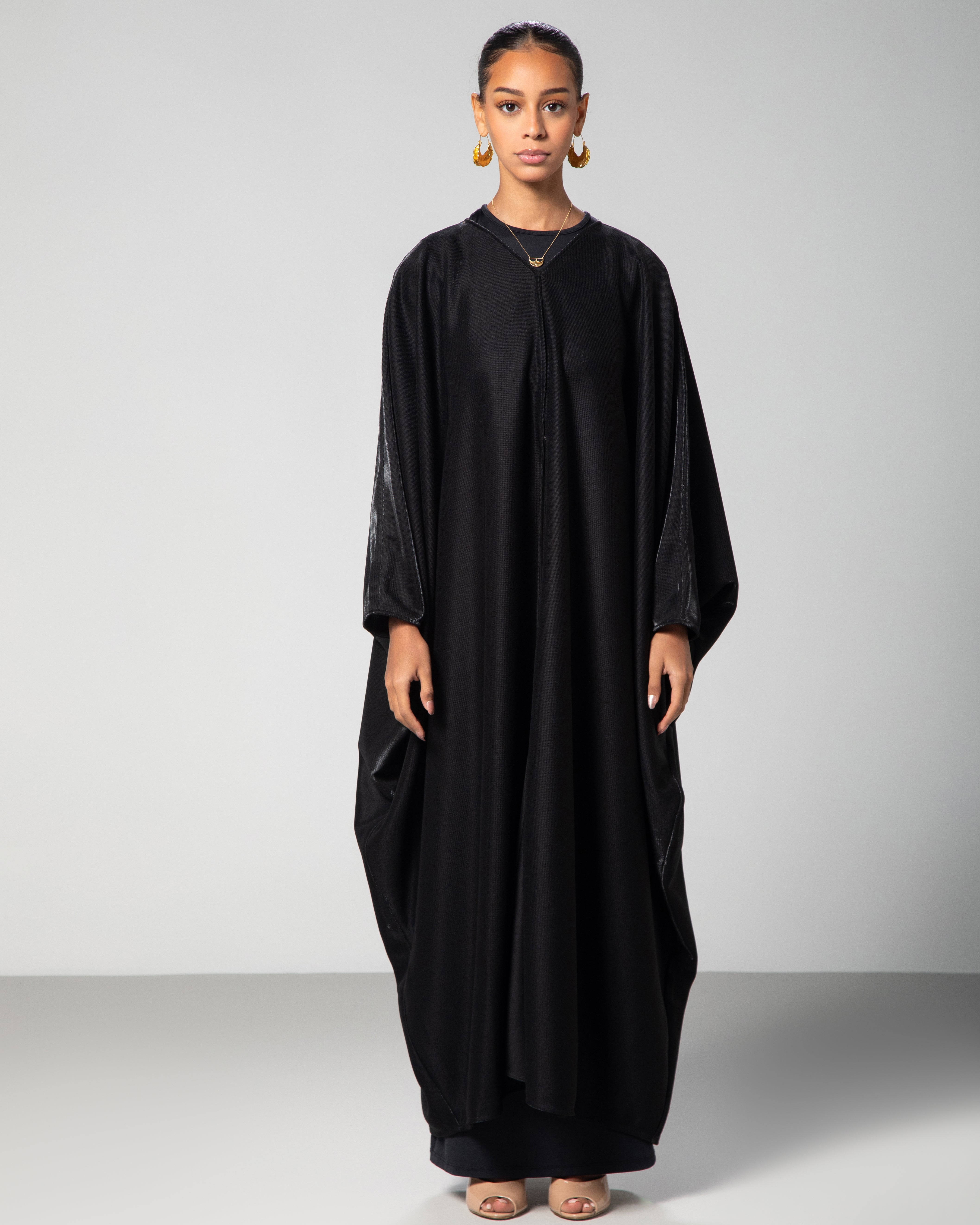 Elegant black abaya cover-up with subtle shimmer, worn by model standing against light grey background — modern modest fashion by Omni The Label KSA UAE Qatar