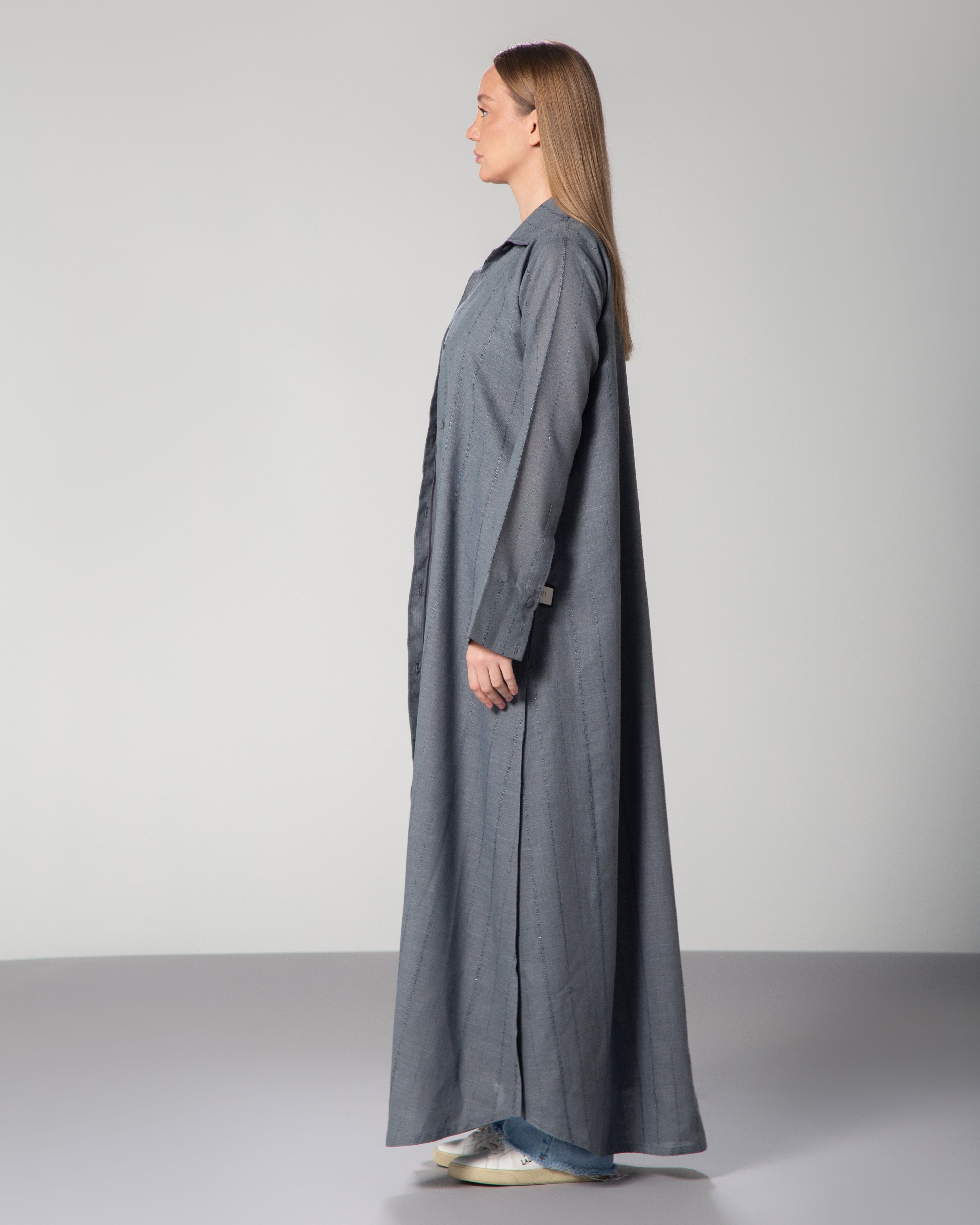 A woman wearing a blue linen collared abaya with sequins, featuring a A-line cut and fabric-covered buttons middle east saudi kuwait qatar uae modest fashion