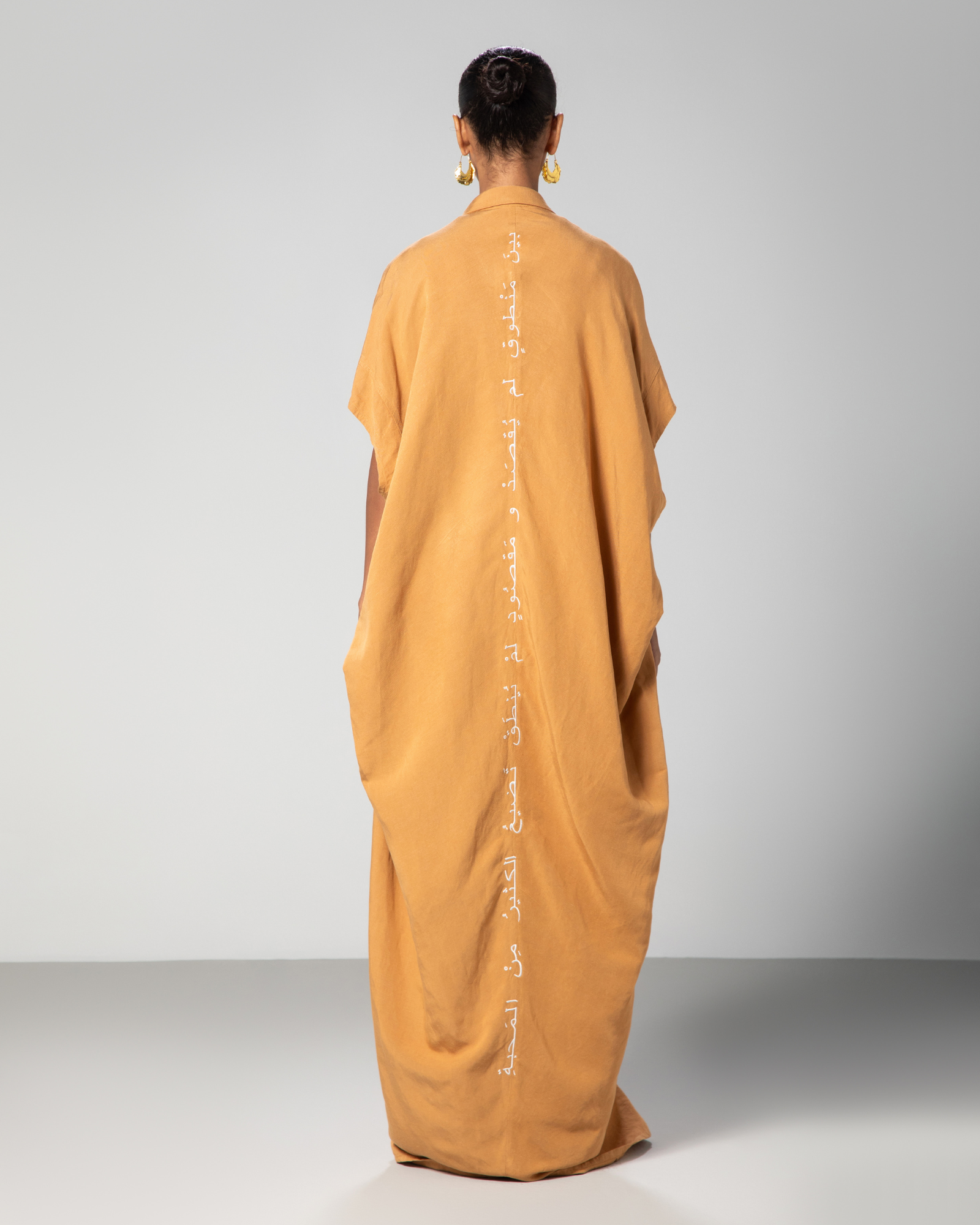 A person wearing a camel brown kaftan with Arabic embroidery on the back.