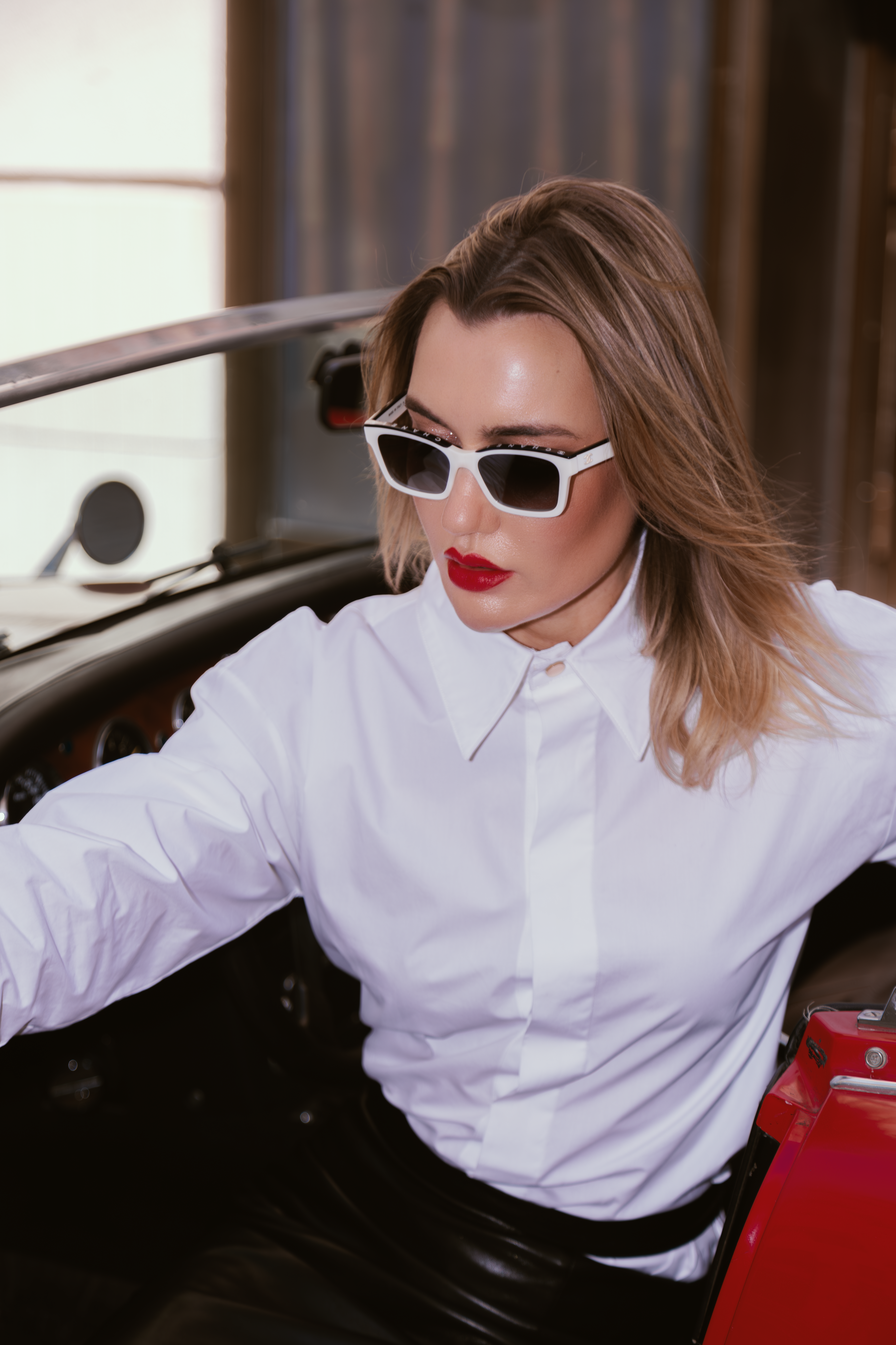 Woman wearing sunglasses and a white shirt inside a vehicle.