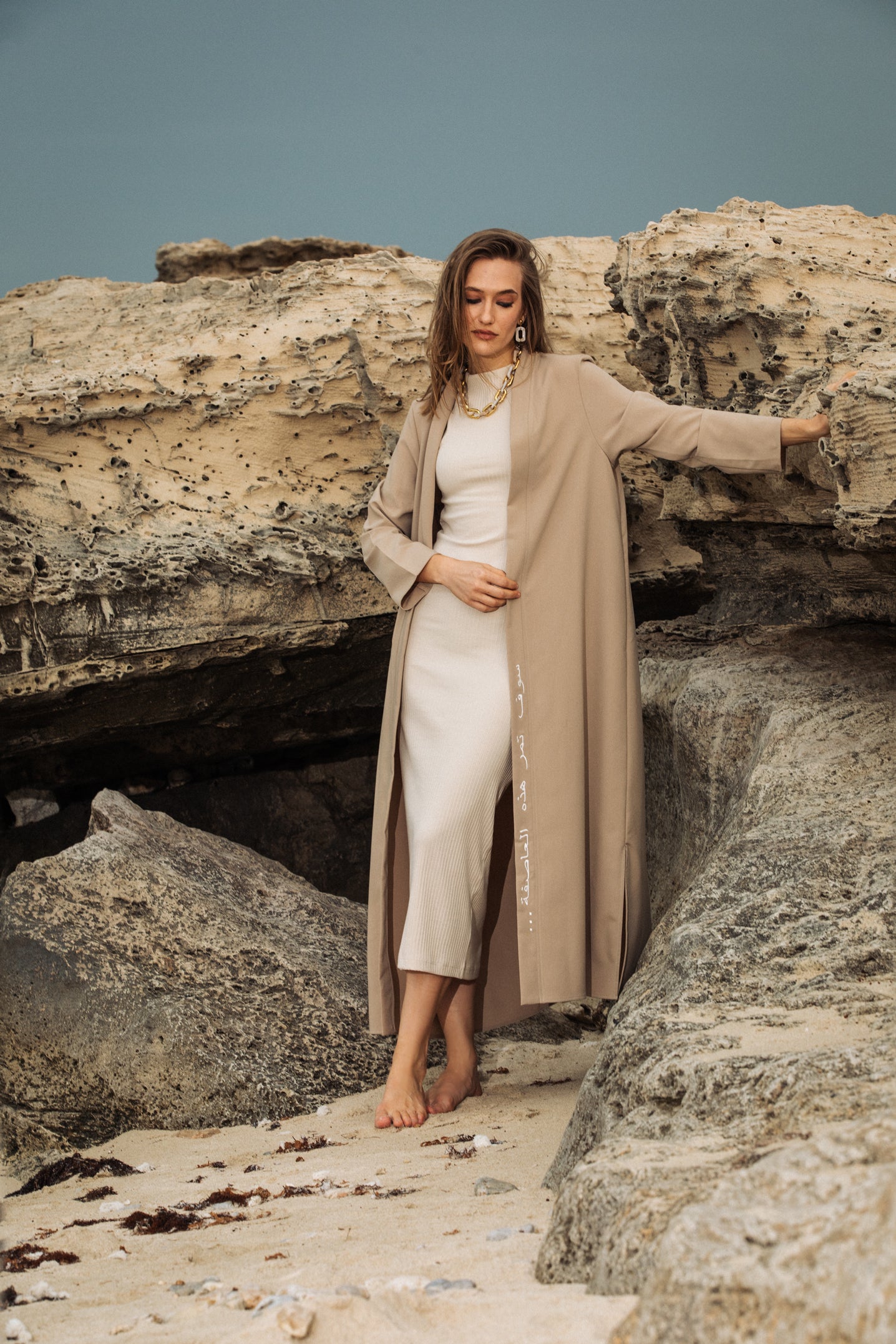 Nude embroidered kimono worn outdoors near rocky beach, styled for resortwear elegance uae ksa qatar