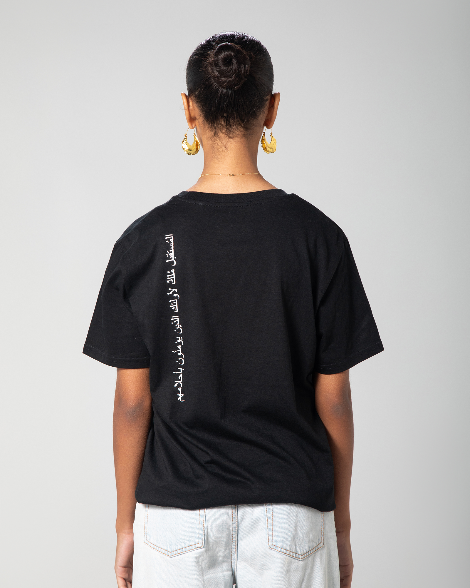 A person wearing a black oversized T-shirt with text on the back, paired with light-colored pants
