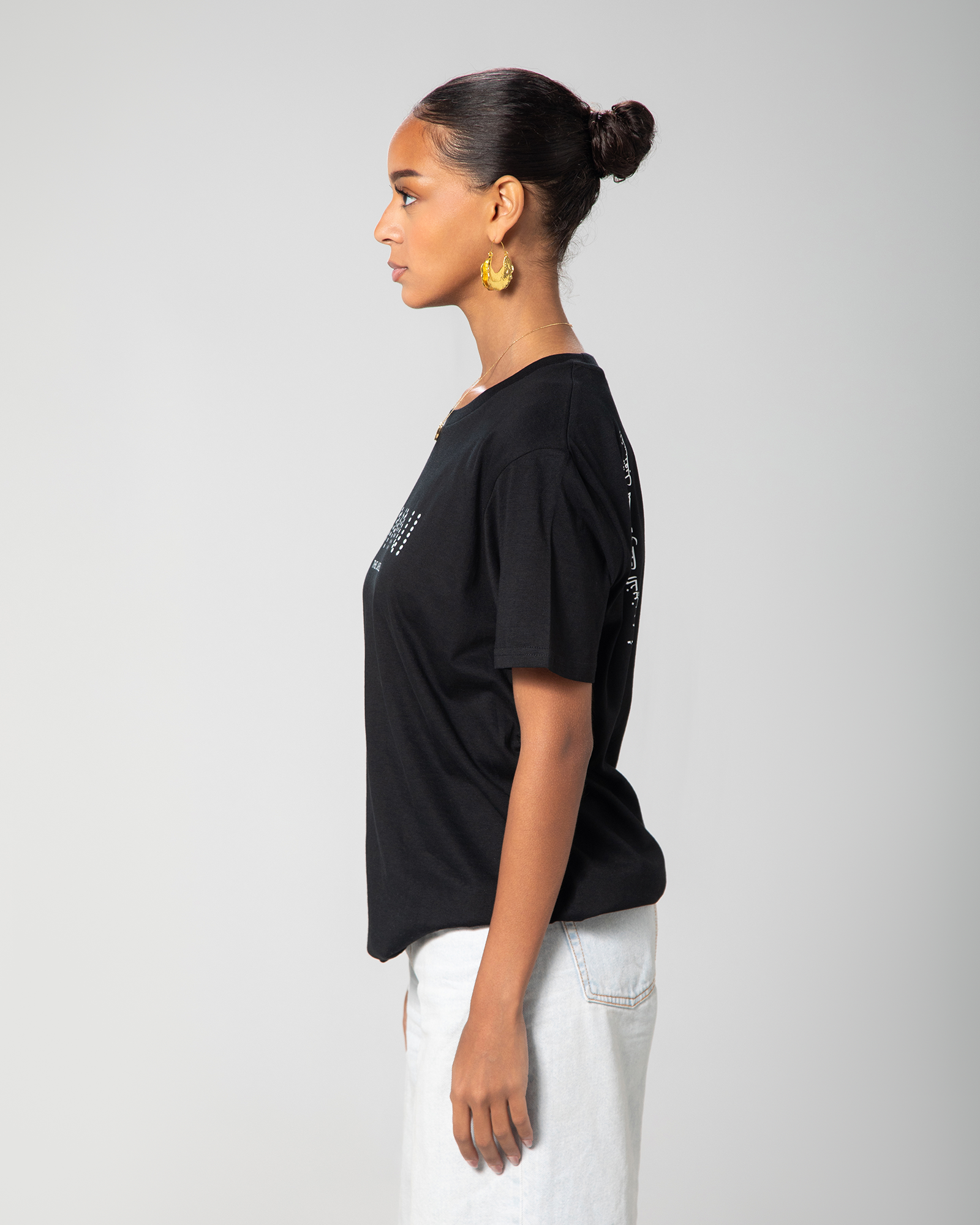 Side profile of a woman wearing a black slim-fit T-shirt by Omni The Label, showing its structured shape and precise short sleeve cut.