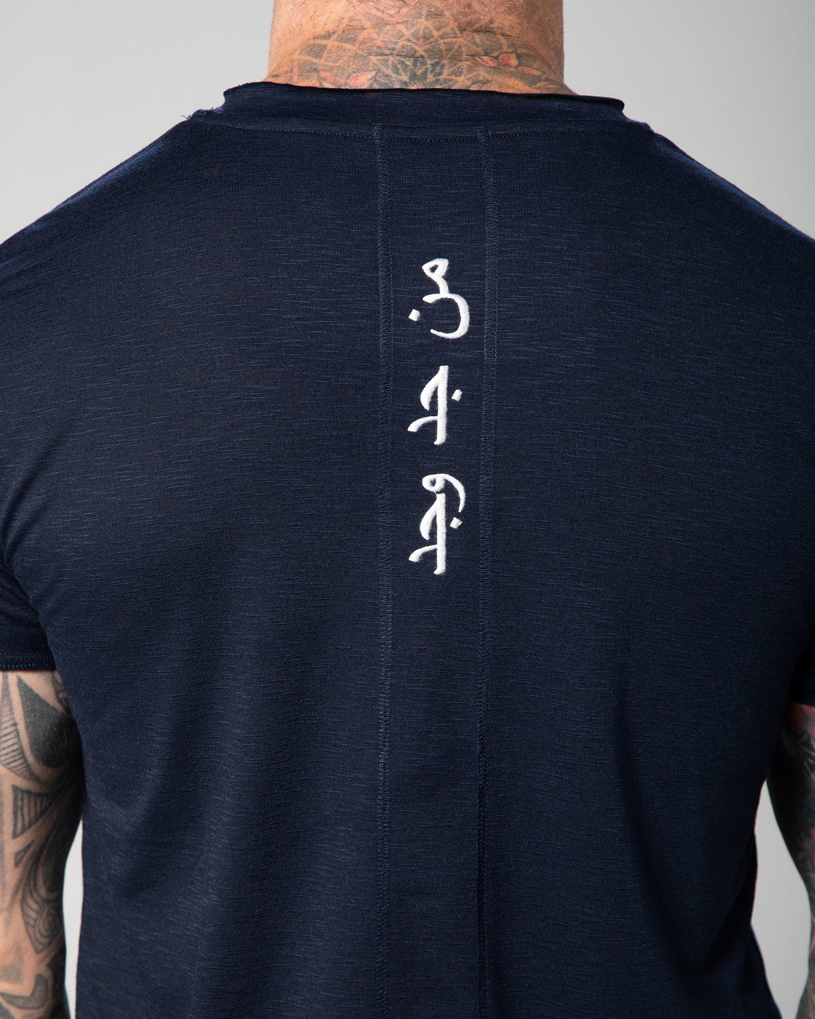 Rear close-up of the Marbella T-shirt in blue with white Arabic embroidery that reads “Who seeks, finds,” positioned vertically for a bold yet refined look UAE KSA Qatar