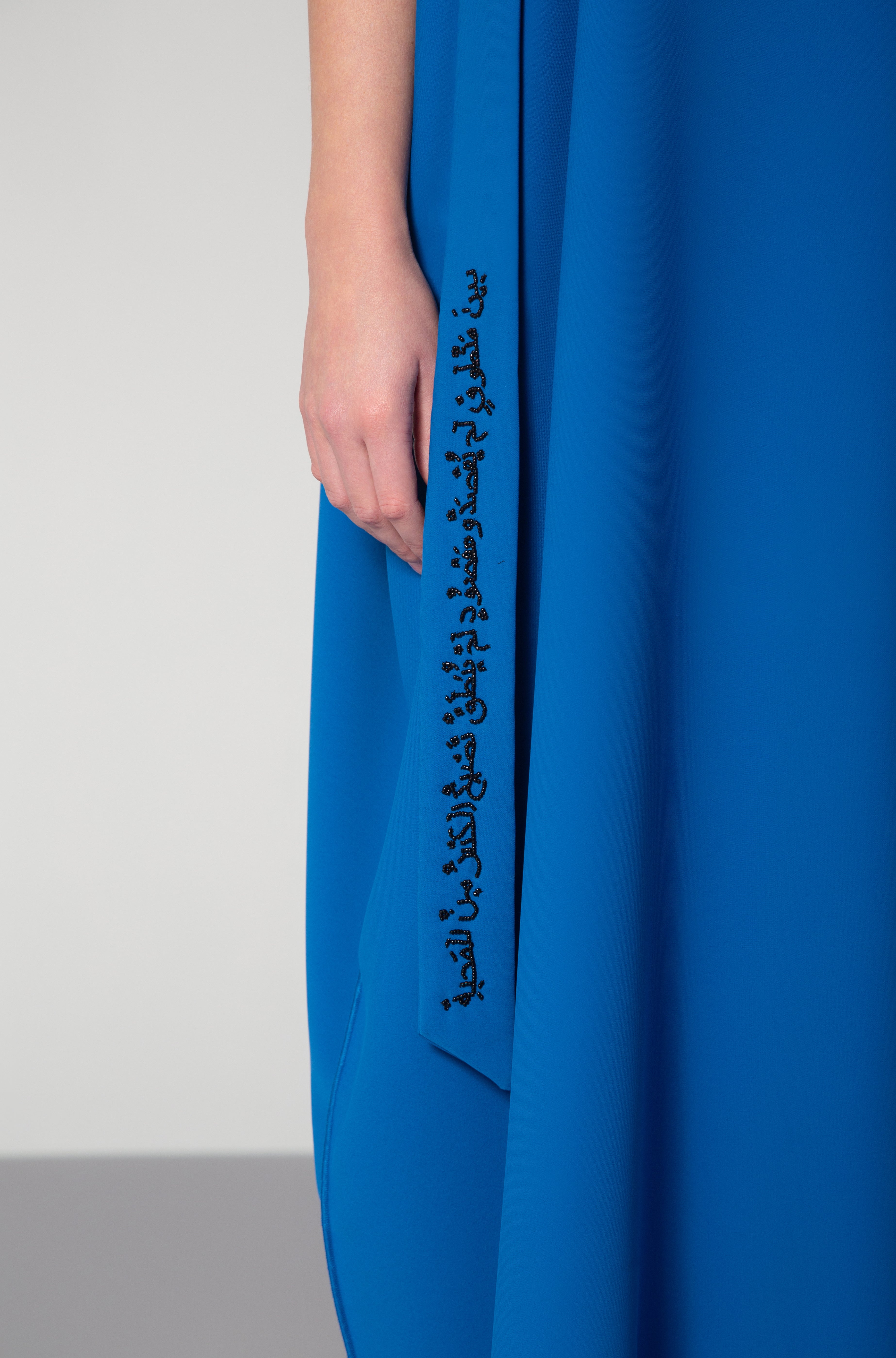 Zoomed view of black Arabic script embroidery on side panel of royal blue dress by Omni The Label designed for culturally rich fashion in Qatar UAE KSA
