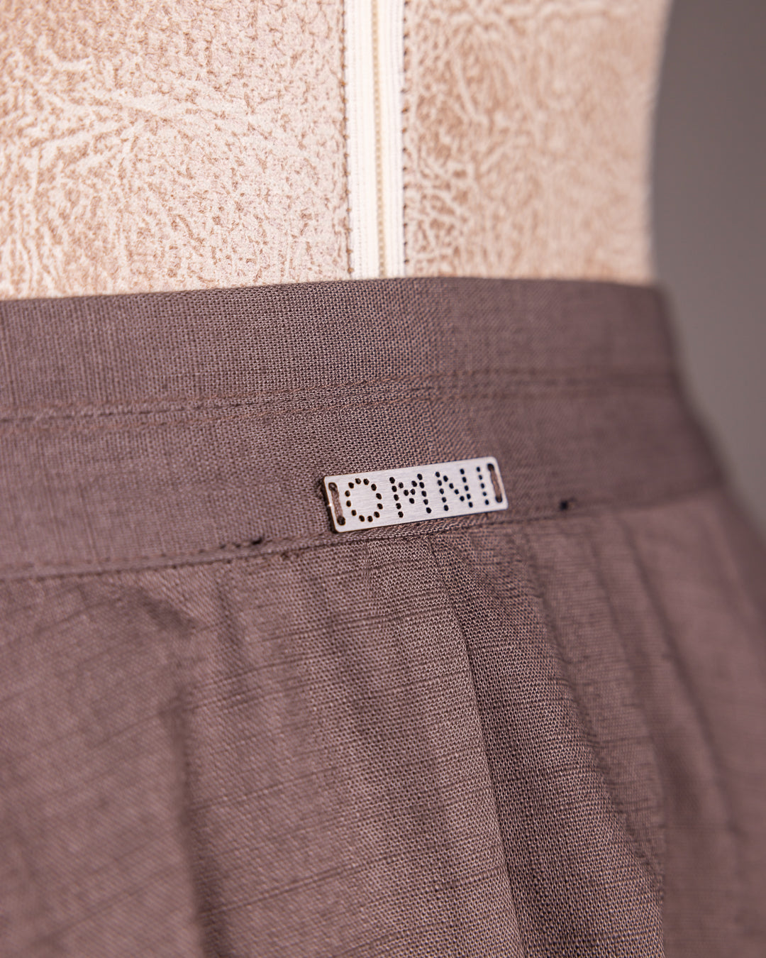 Minimalist image showing Omni The Label metal logo tag on soft brown fabric – Qatar KSA UAE