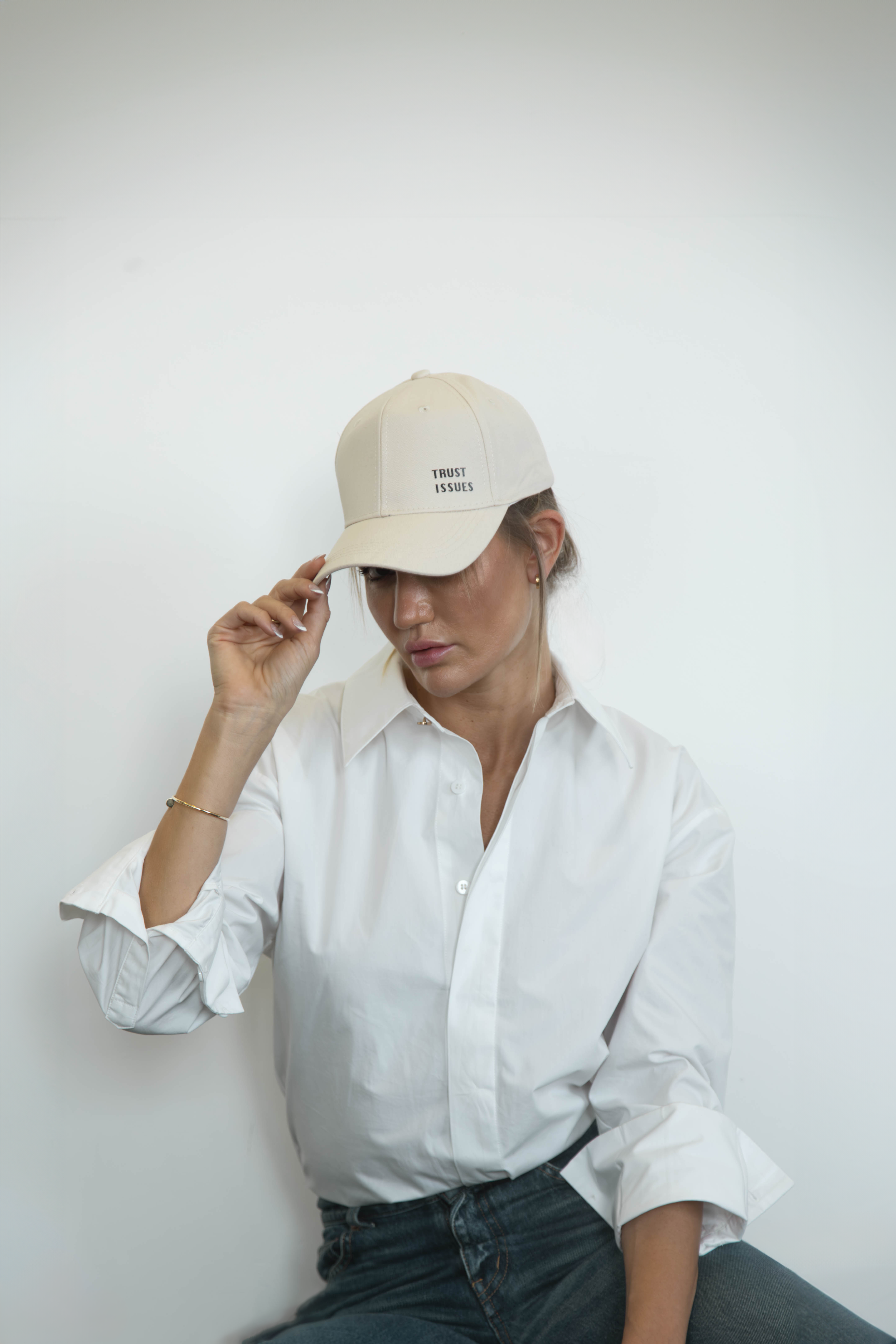Person wearing a beige cap and white shirt by Omni The Label against a plain background