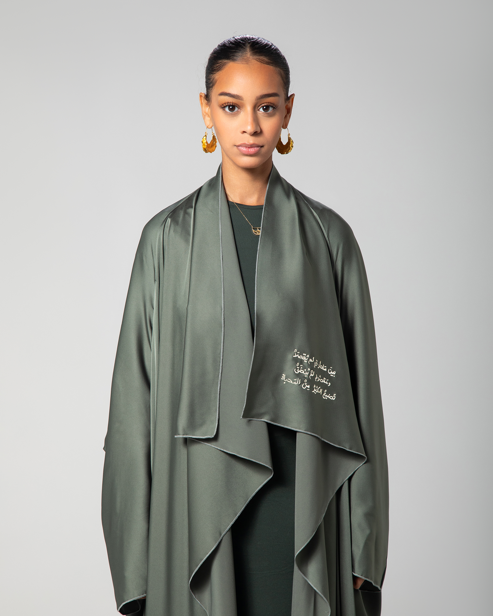 Model wearing green Flow Abaya with front closed, standing against grey background – UAE, KSA, Qatar