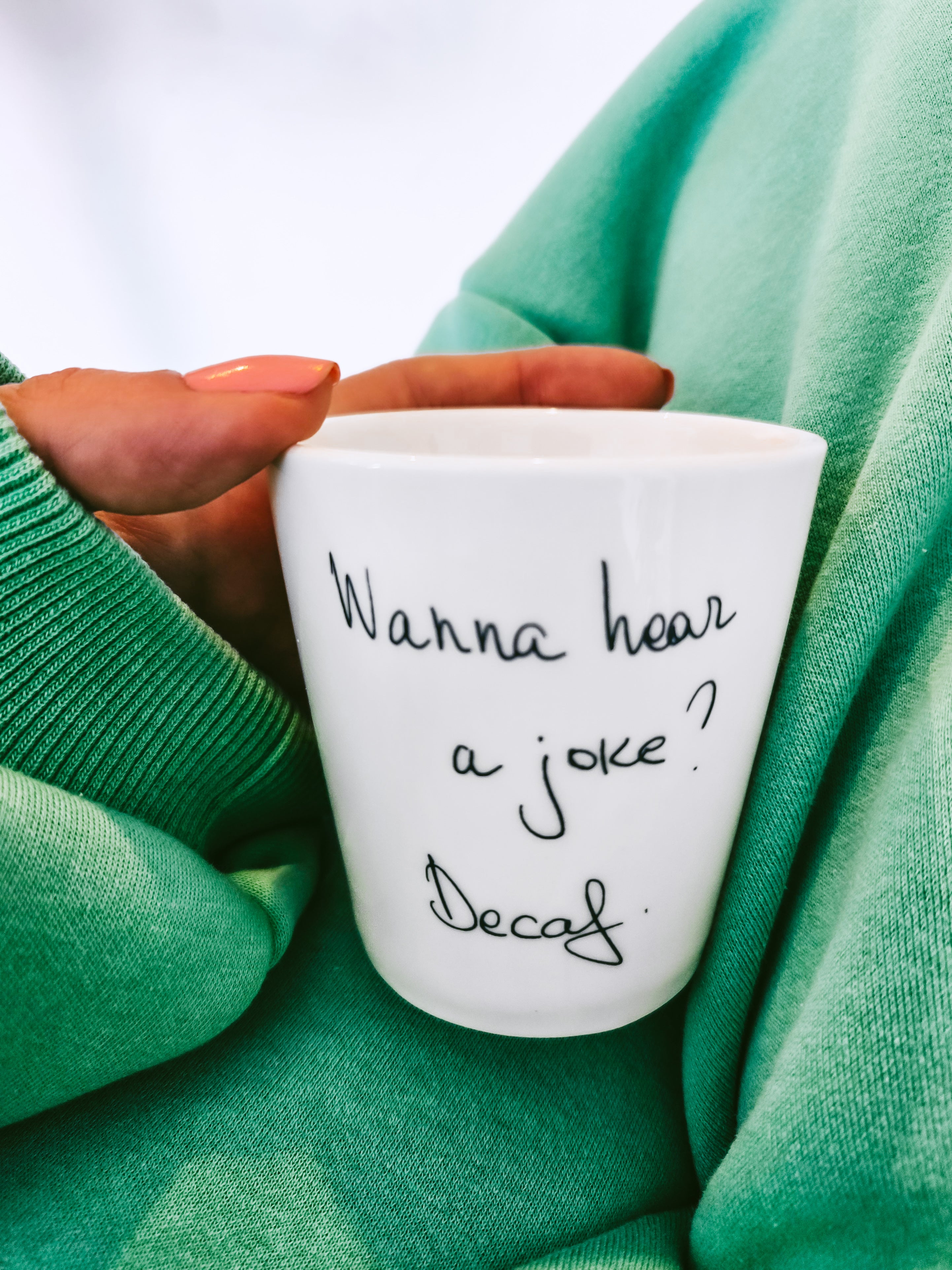 A white china coffee cup with the text 'Wanna hear a joke? Decaf' written on it,