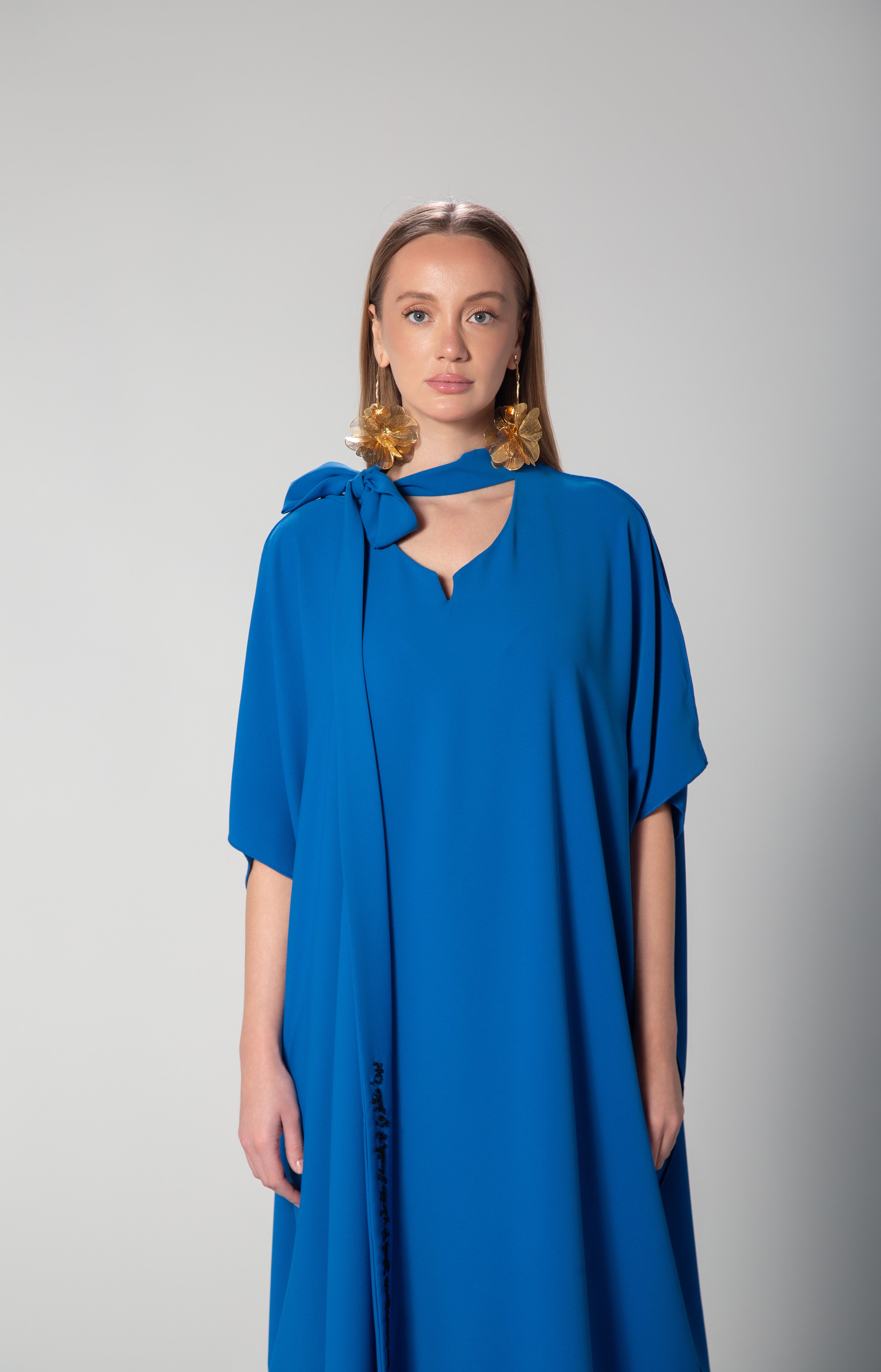 Front view of woman wearing royal blue dress with statement bow collar and Arabic embroidery on sleeve by Omni The Label modest fashion style for Qatar UAE KSA