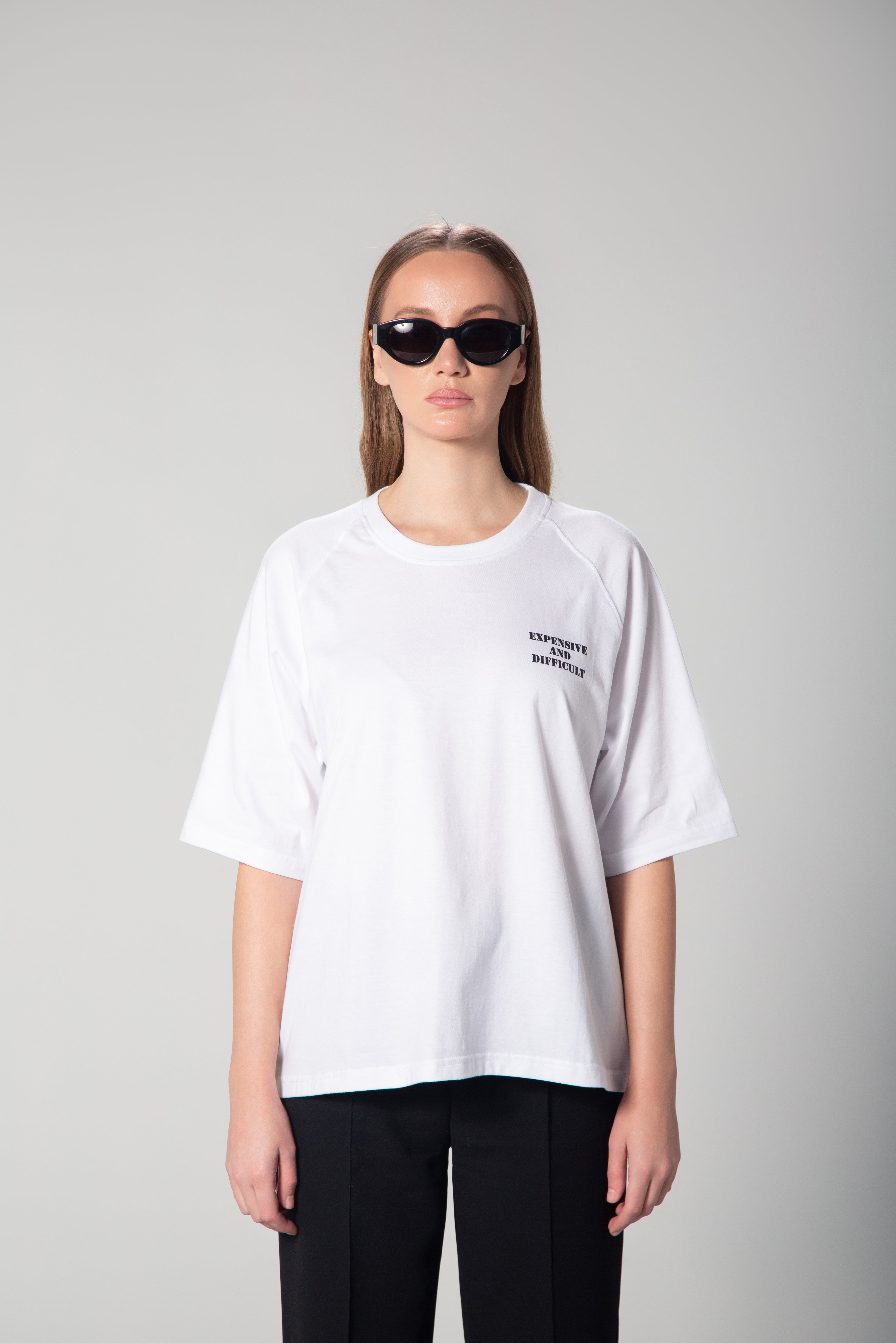 A white oversized t-shirt with the words Expensive and Difficult printed in bold, contrasting lettering on the front. The relaxed fit and dropped shoulders give it a modern, effortless look. Perfect for casual and statement styling.