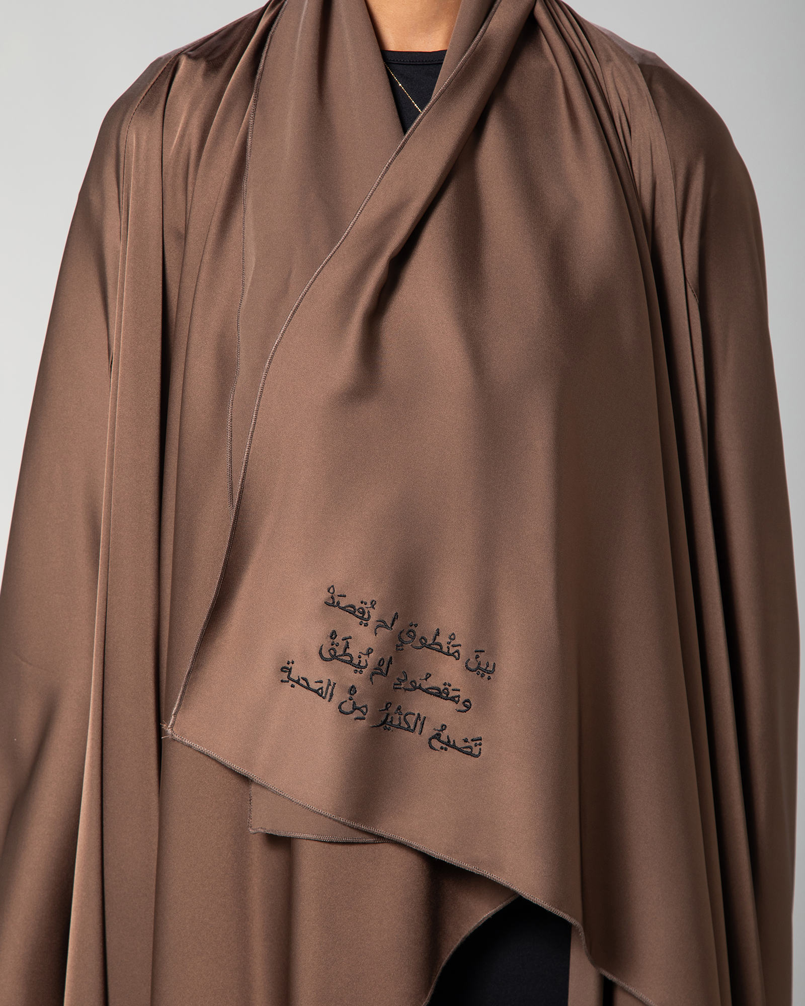 Close-up of the front Arabic embroidery on the Flow Abaya in brown by Omni The Label, displaying the quote: “Between what was said and not meant and what was meant but not said, most love is lost,” stitched in elegant black calligraphy KSA UAE Qatar