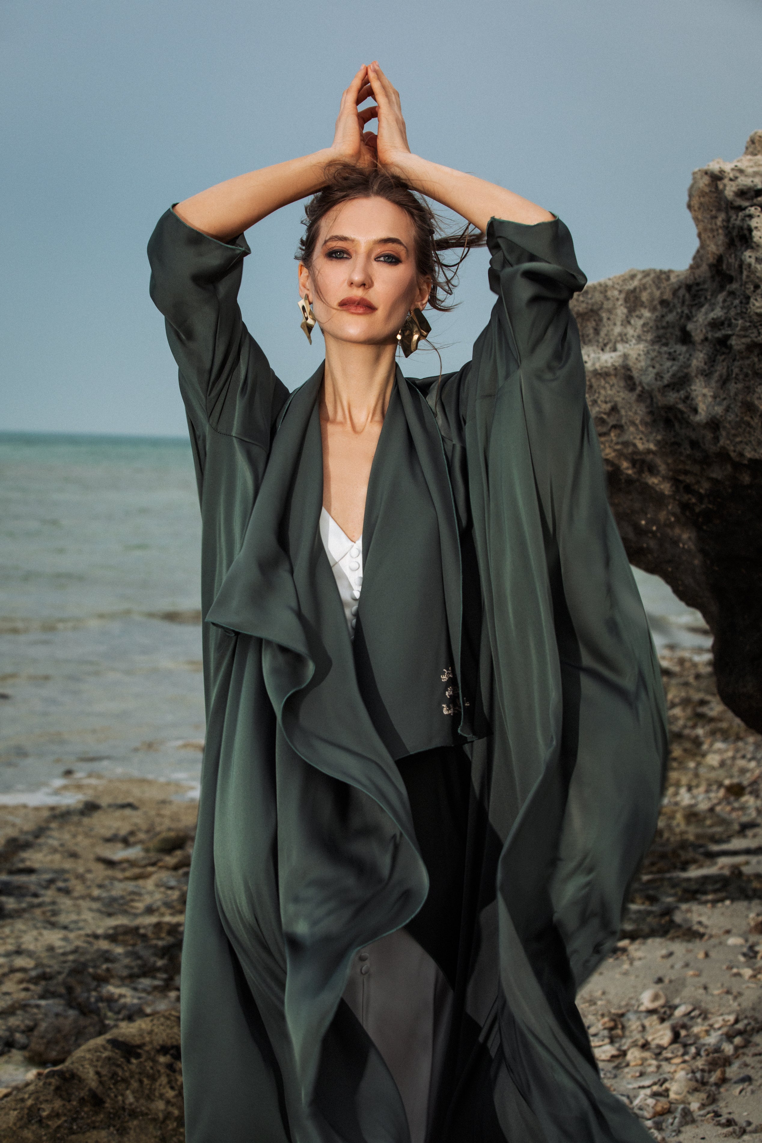 Model outdoors in Omni The Label’s Flow Abaya in green with arms raised slightly – UAE, KSA, Qatar