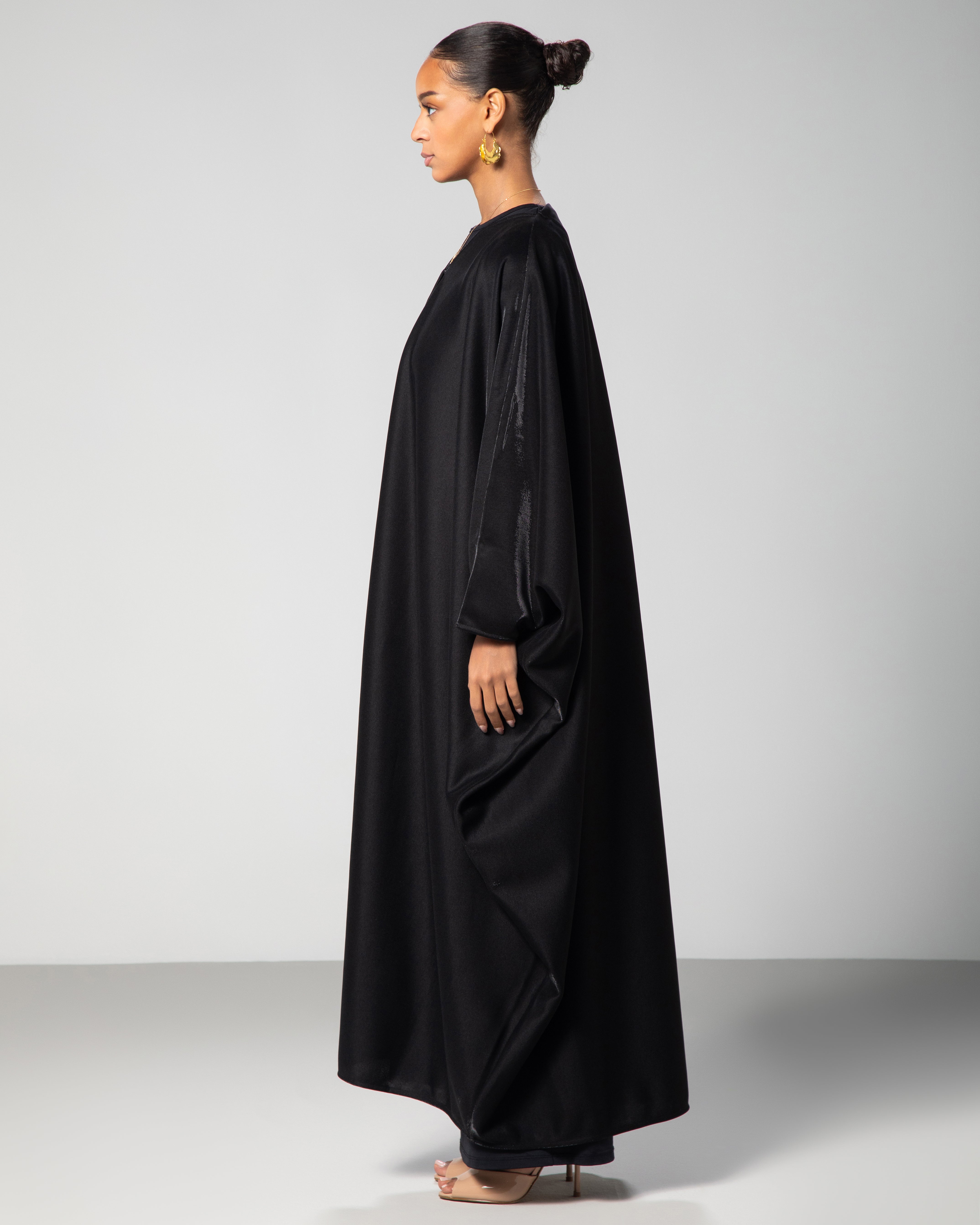 Black abaya with soft sheen and draped design, modeled in studio setting — modern Islamic fashion by Omni The Label KSA UAE Qatar