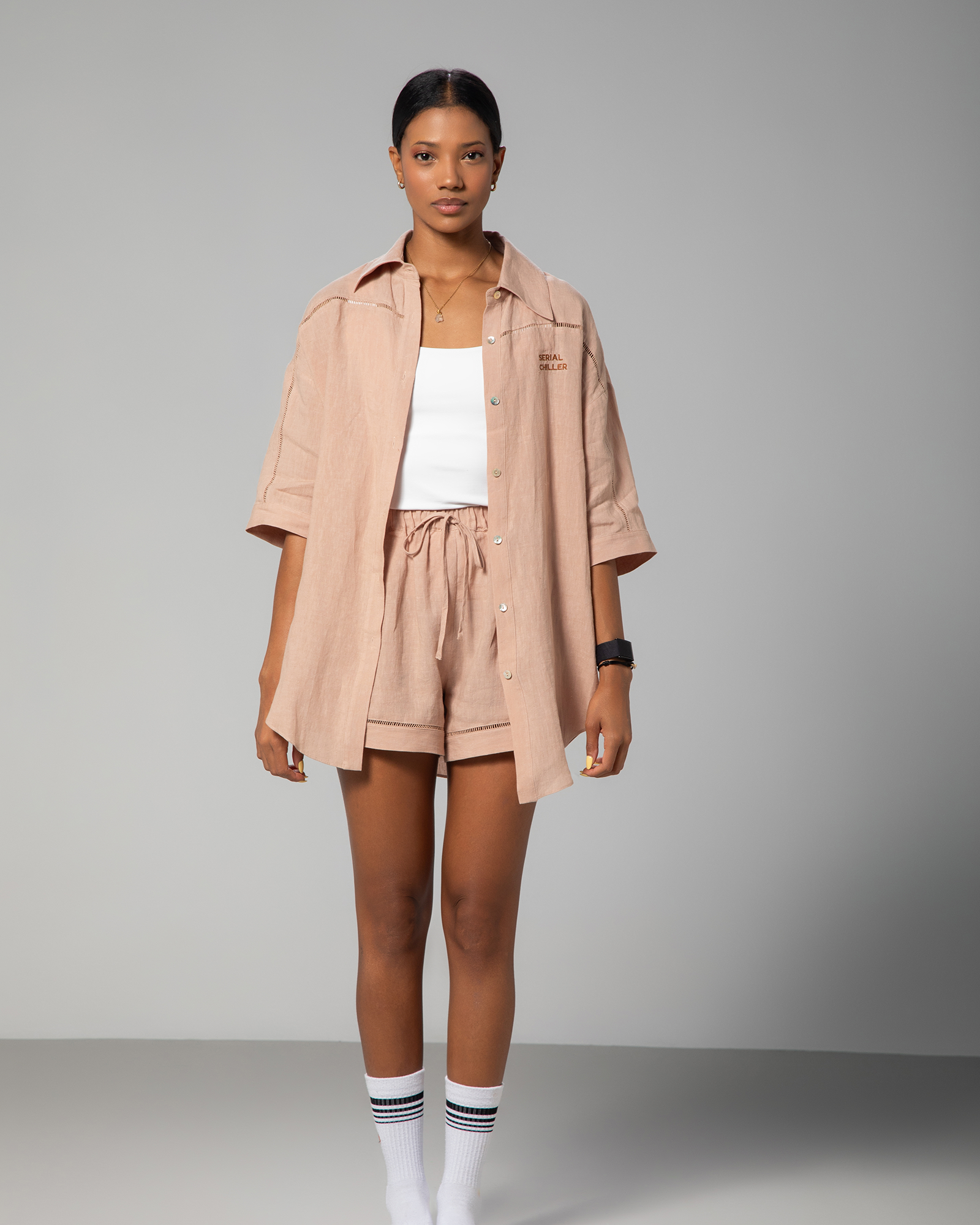 Woman wearing a nude linen co-ord set with short-sleeve shirt and drawstring shorts from Omni The Label, styled with a white top for a minimal summer look UAE KSA Qatar