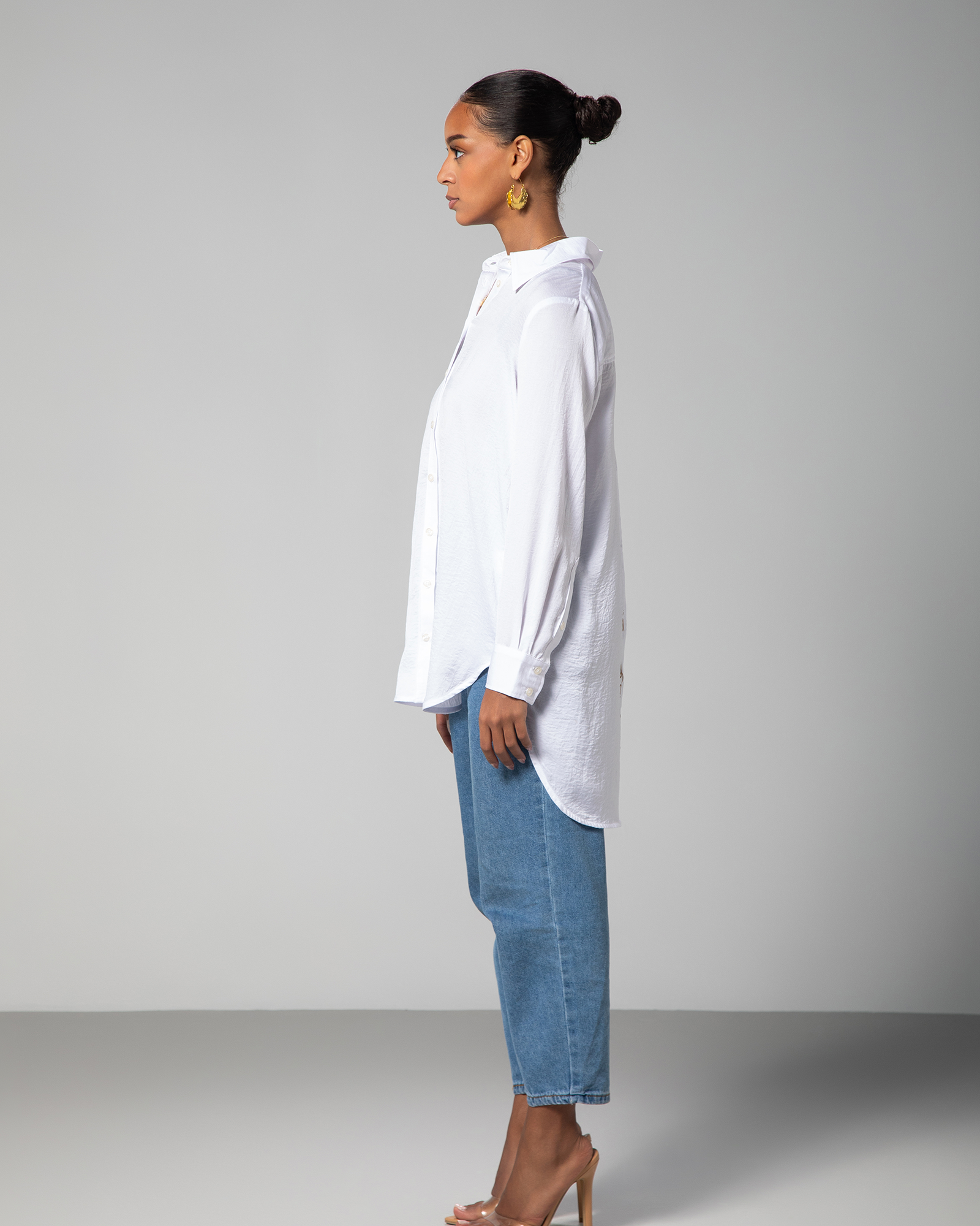 Side profile of model wearing Omni The Label’s white shirt with extended hem fashion-forward look worn across KSA UAE Qatar