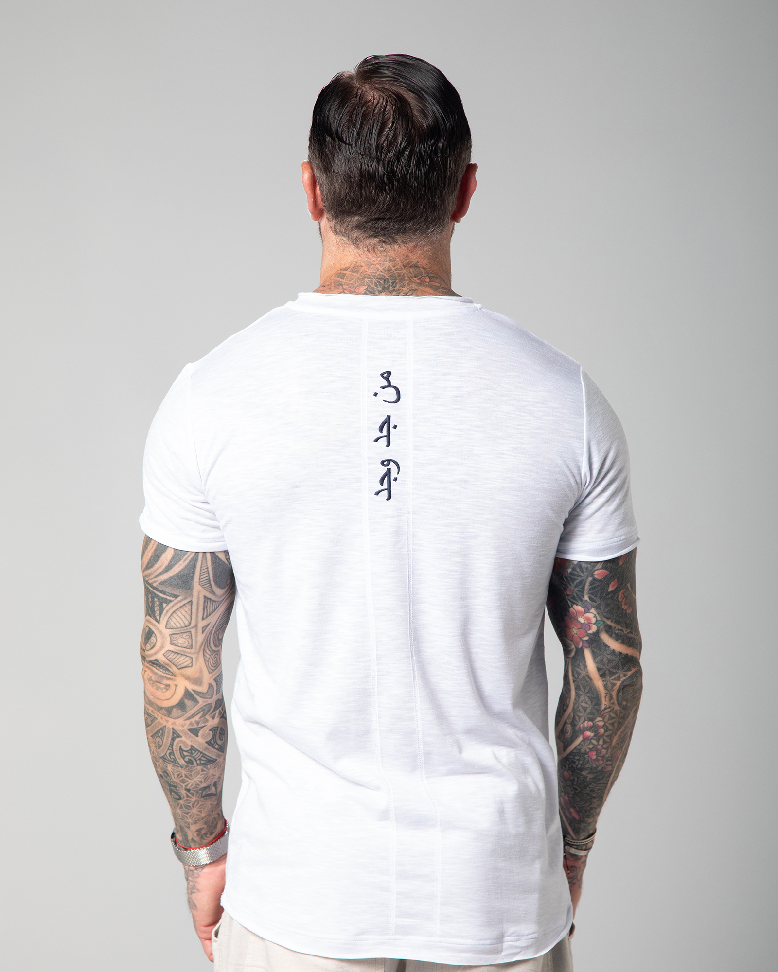 Back view of the Marbella white T-shirt featuring vertical Arabic embroidery that translates to “Who seeks finds.”UAE, KSA, Qatar