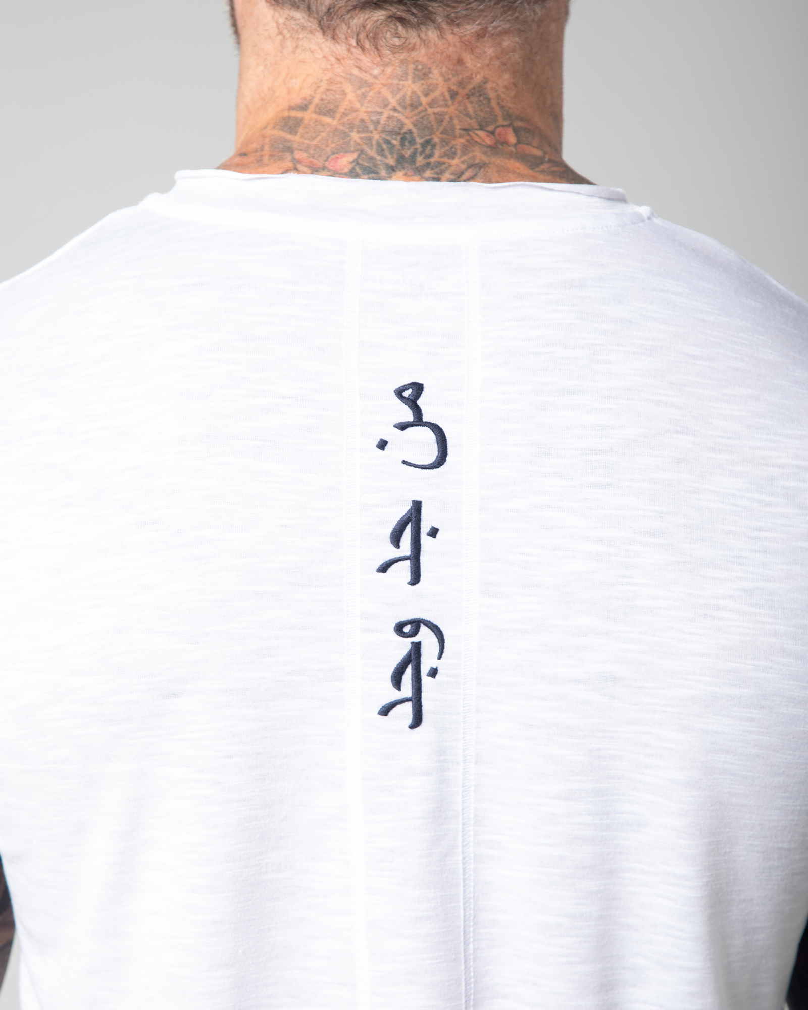 back view of the Marbella white T-shirt featuring vertical Arabic embroidery with the phrase “Who seeks, finds.”UAE, KSA, Qatar