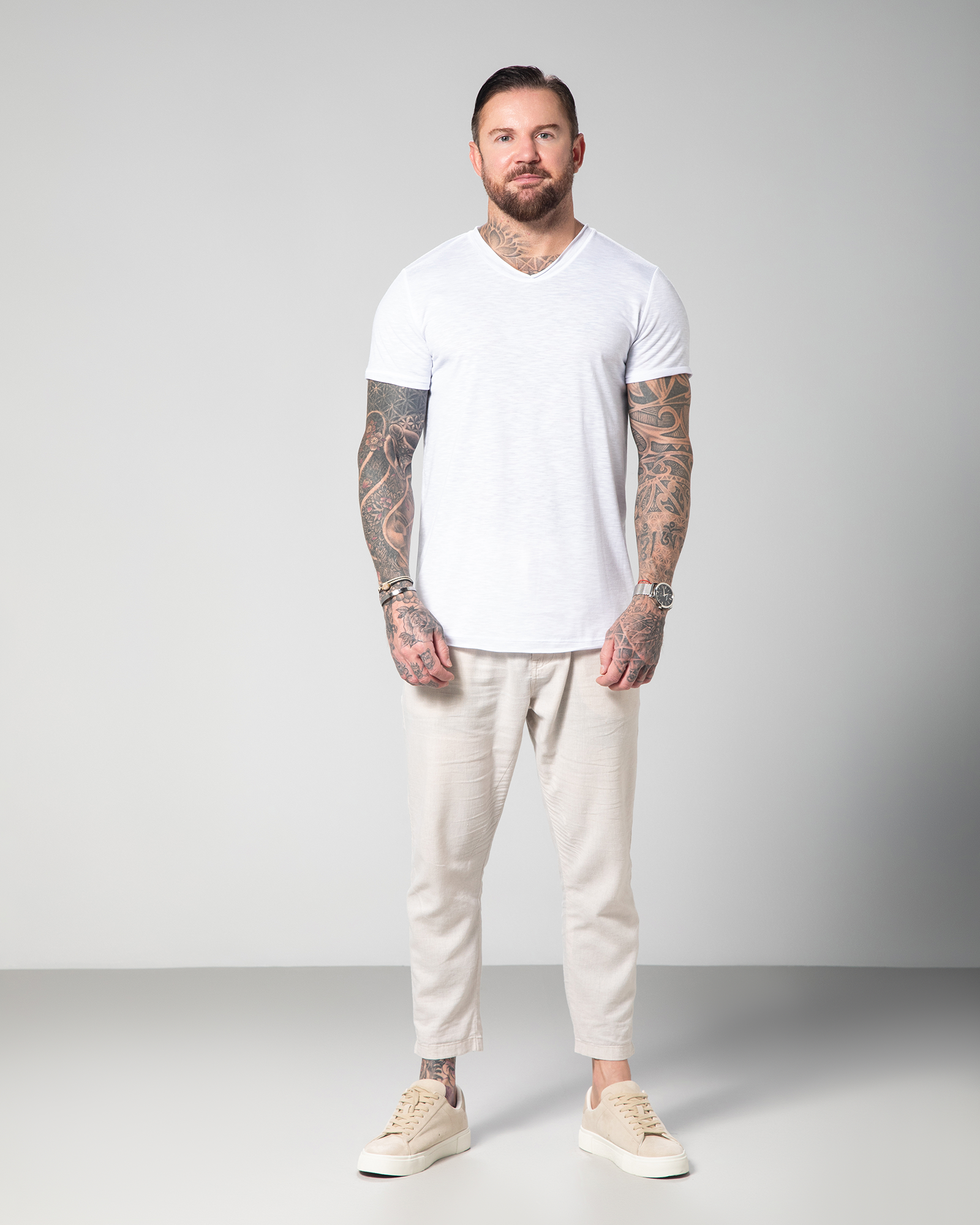 Male model wearing the Marbella V-neck T-shirt in white by Omni The Label, made from 100% slub jersey for breathable, lightweight comfort.UAE, KSA, Qatar