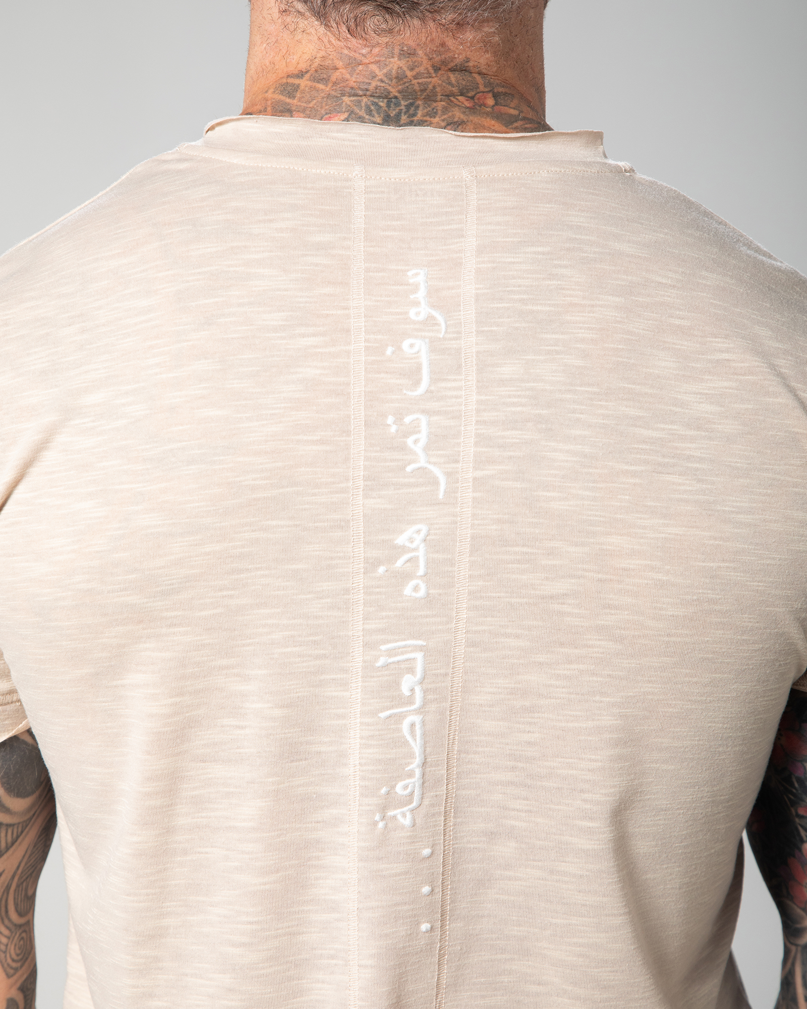 Close-up of the Marbella nude T-shirt showcasing vertical Arabic calligraphy reading “this too shall pass,” embroidered with intention for a meaningful finishing touch UAE KSA Qatar