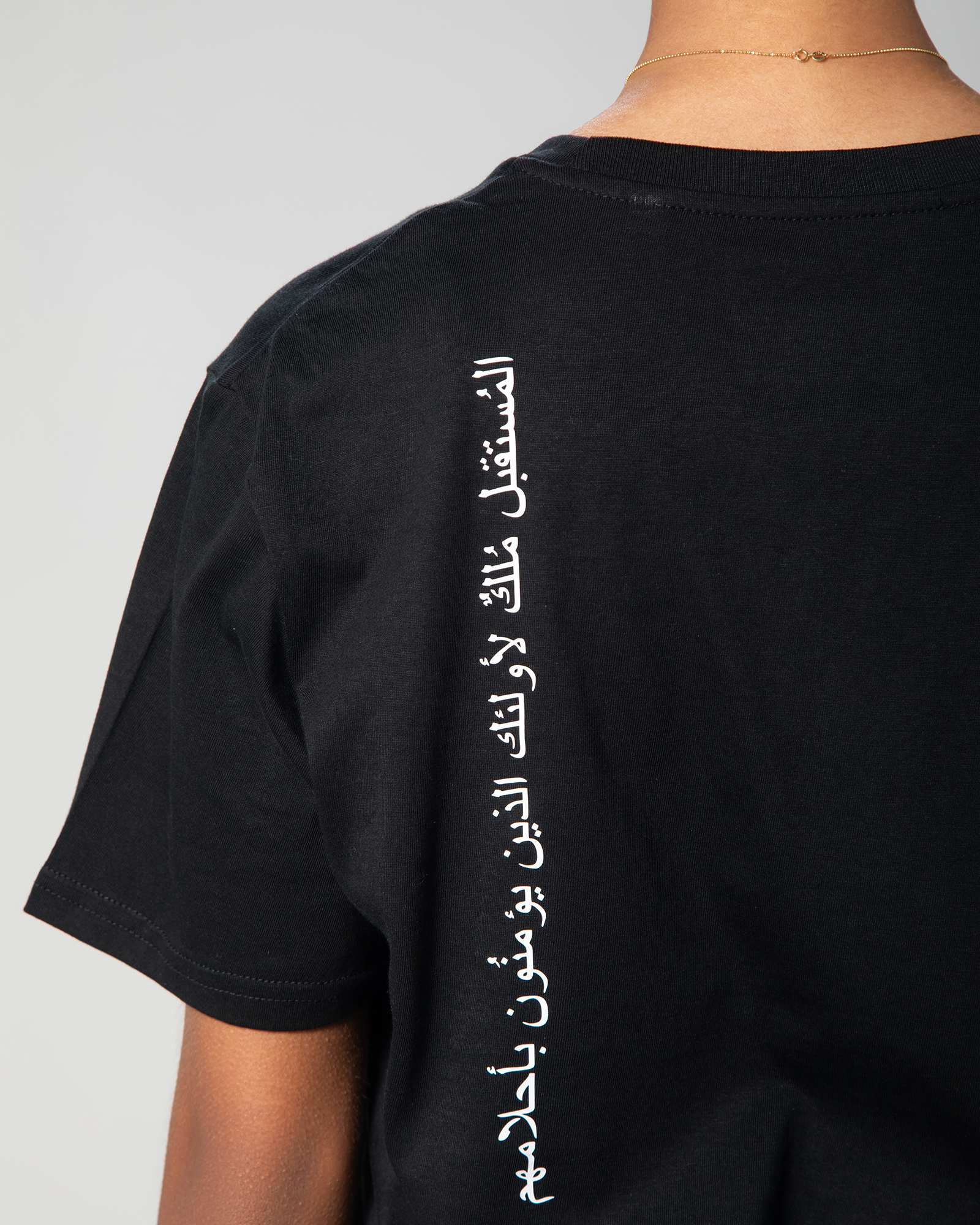 Close-up of white Arabic calligraphy print vertically aligned on the back of Omni The Label’s black T-shirt, delivering an inspiring message.