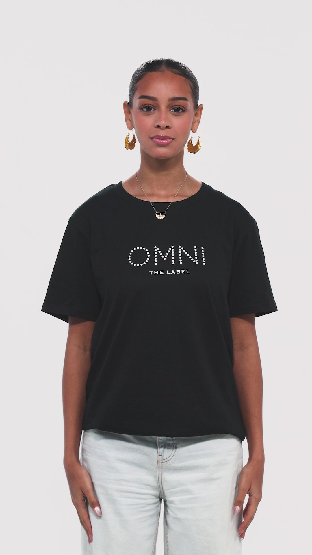 This video showcases Omni The Label’s black fitted T-shirt for women, crafted from soft, breathable cotton with a tailored silhouette. The model highlights all angles — front with the minimal chest logo, side fit, and back featuring the Arabic quote print: “The future belongs to those who believe in their dreams.” A statement piece that balances comfort, simplicity, and purpose.