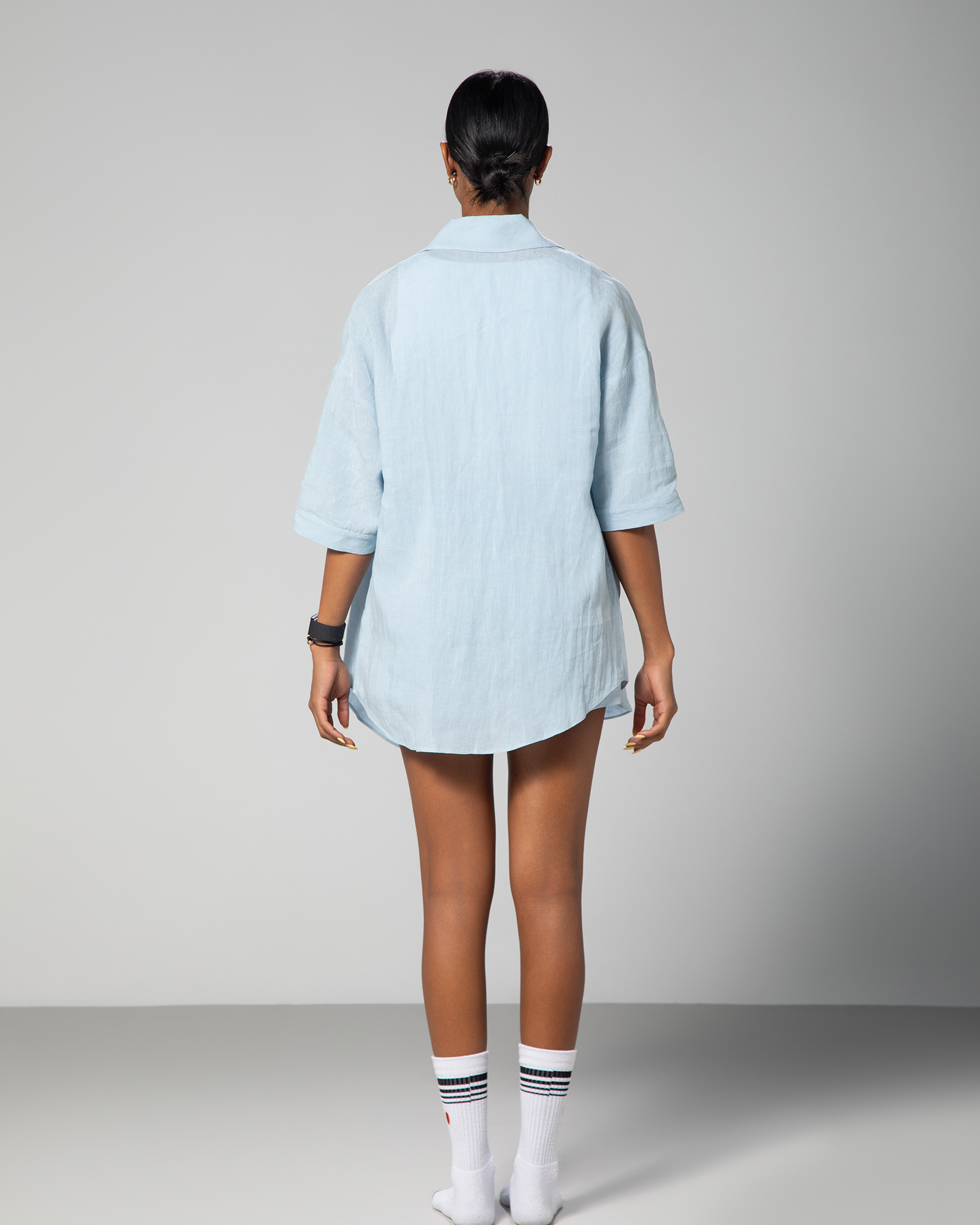 Back view of a woman wearing a baby blue linen co-ord set from Omni The Label, showcasing the relaxed fit and subtle embroidery detail on the shirt, styled for modern summer comfort UAE KSA Qatar