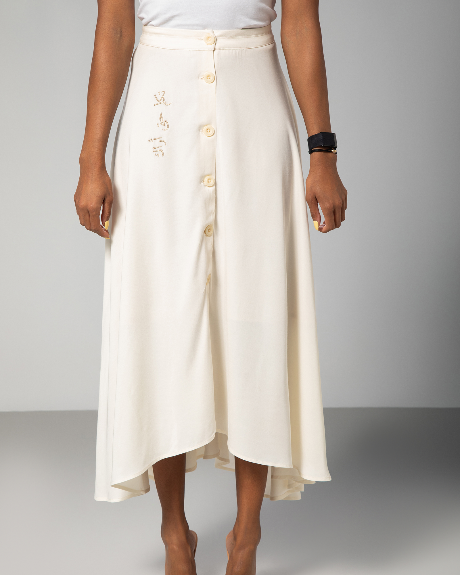 Front view of asymmetric cream skirt with statement Arabic detail, styled with short sleeve top – UAE, KSA, Qatar
