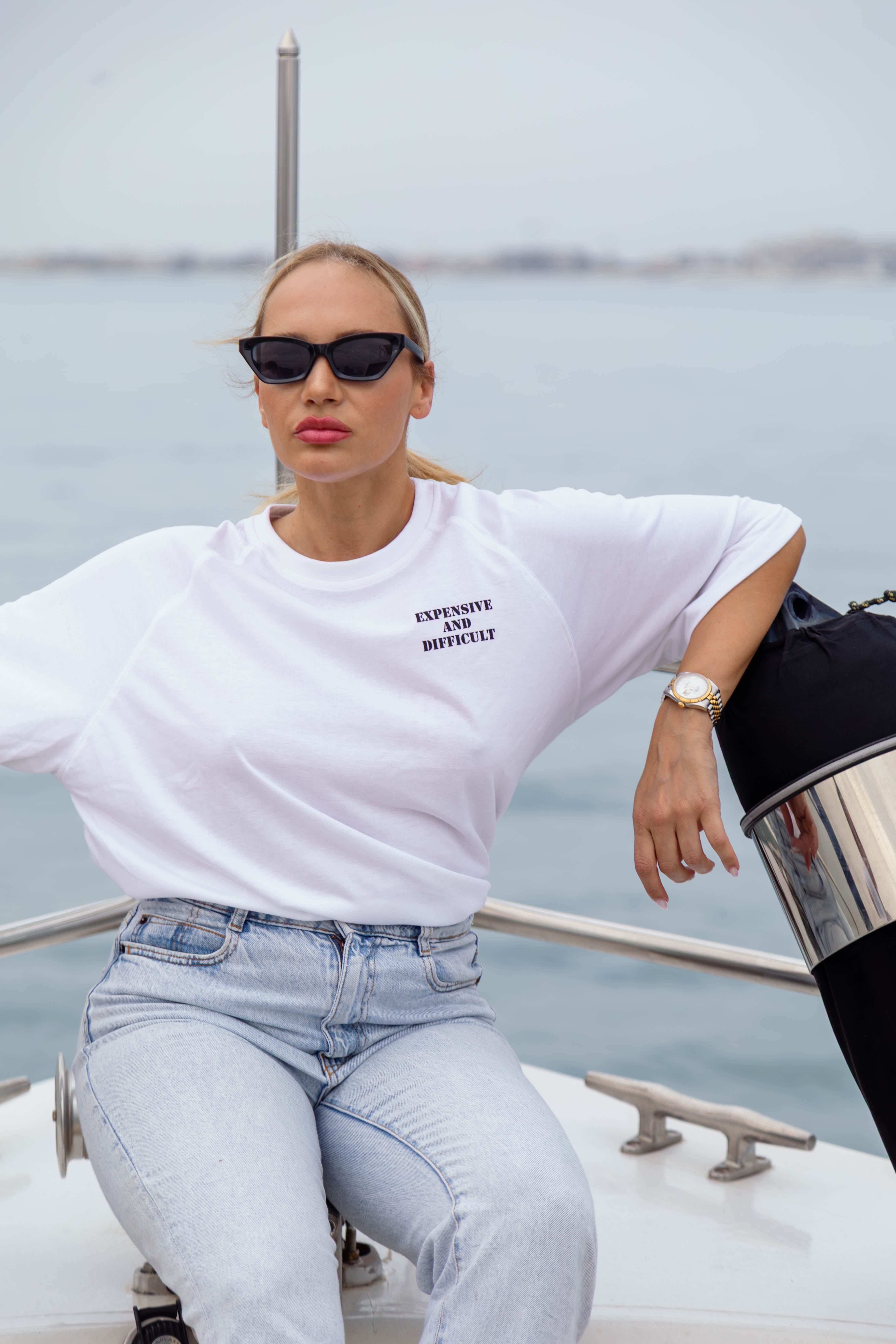 Woman sitting on a boat wearing sunglasses and a white t-shirt with text.