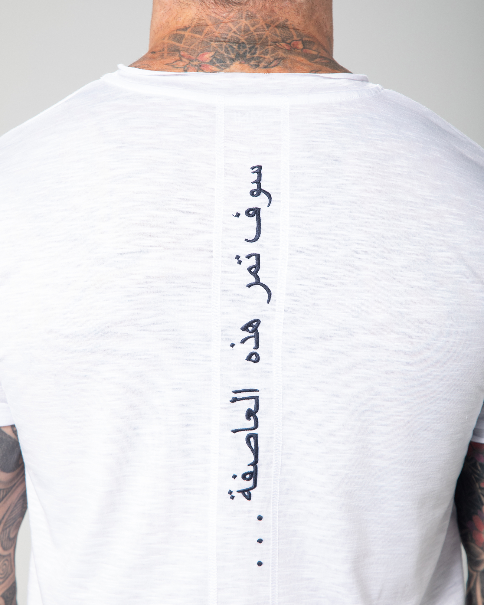 Back embroidery detail of the Marbella white T-shirt with Arabic calligraphy meaning “This too shall pass,” stitched along the spine.UAE, KSA, Qatar