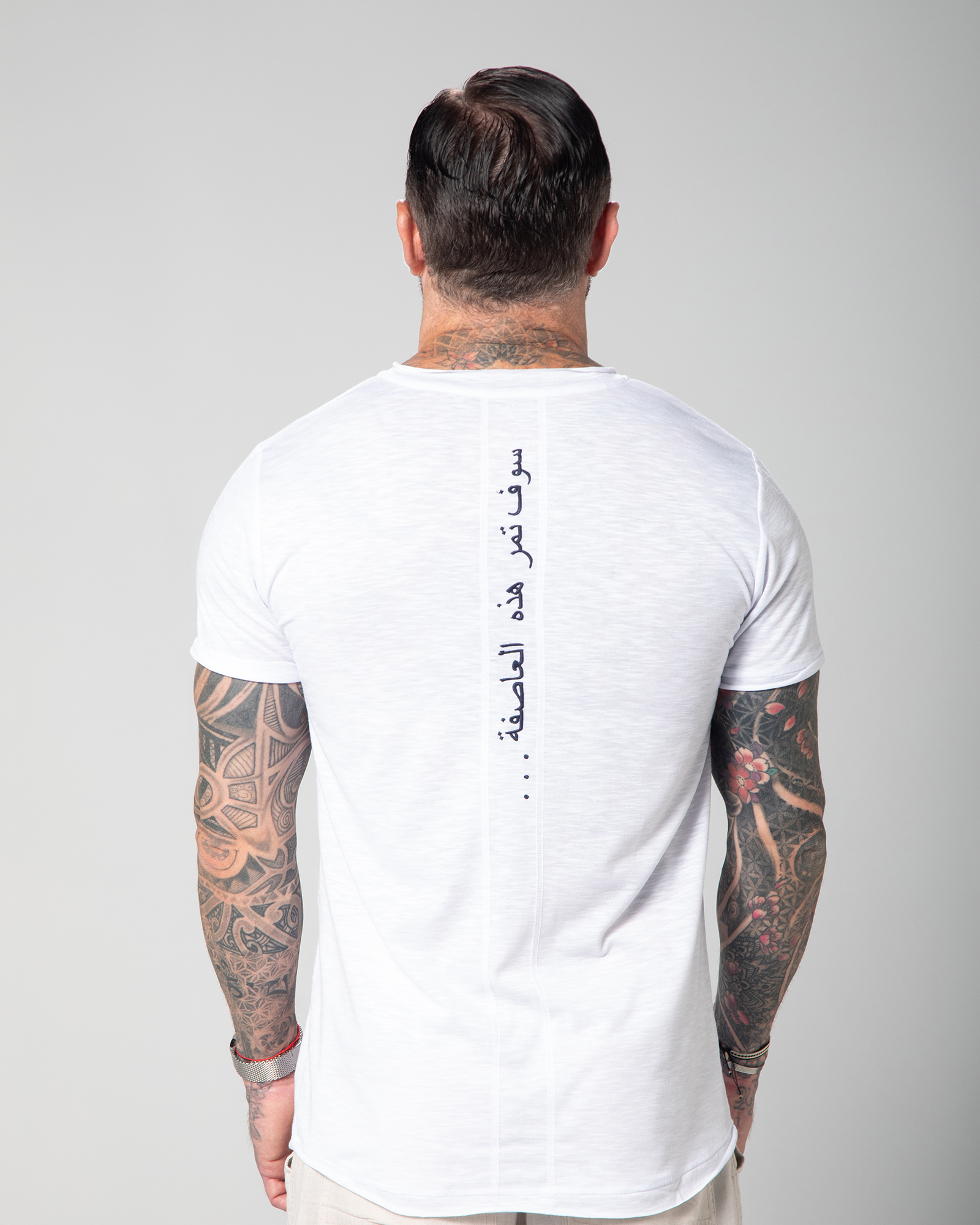 A man wearing a white Marbella V-neck T-shirt with Arabic embroidery on the backUAE, KSA, Qatar
