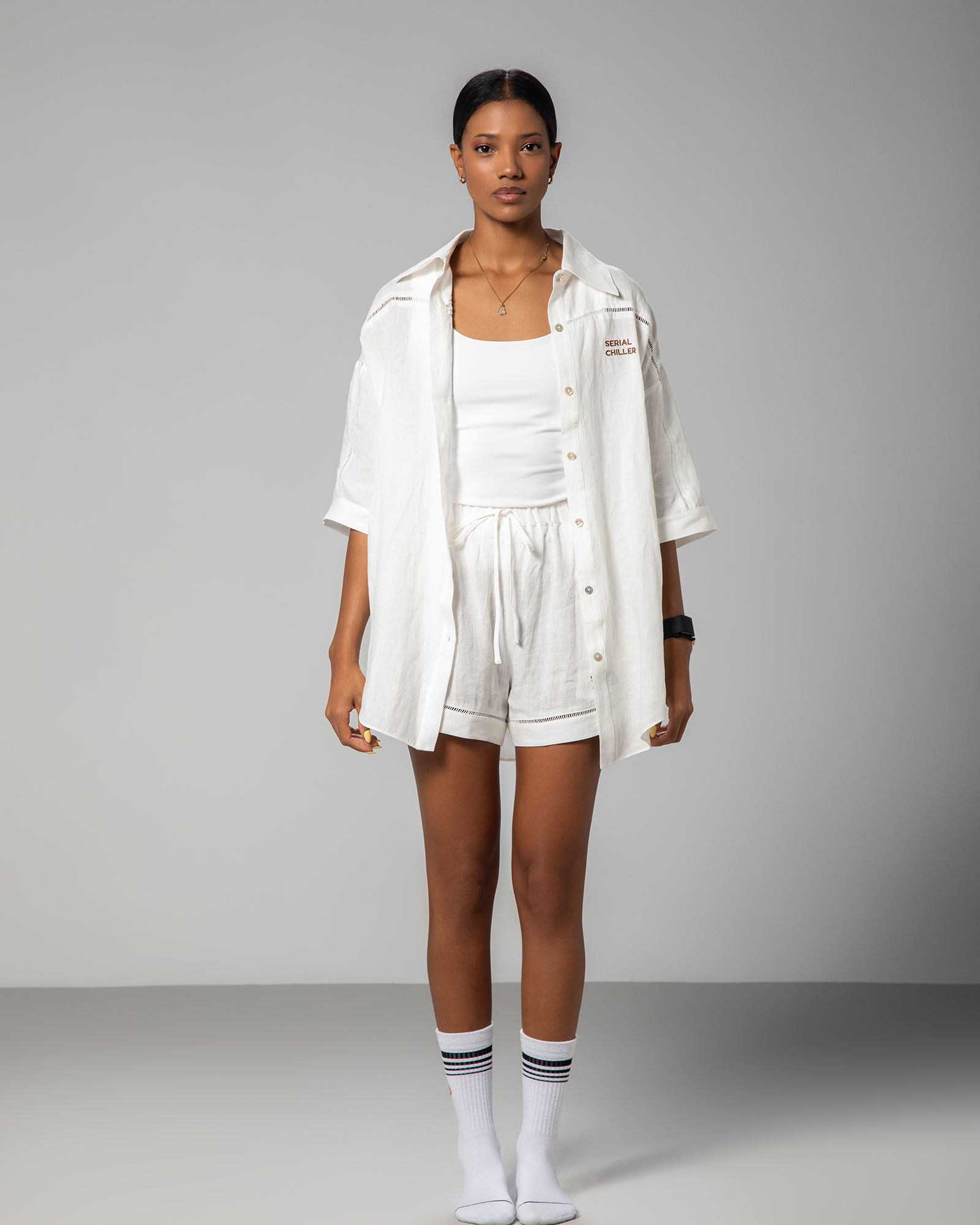 A model wearing a white loose-fit shirt and matching shorts with the text 'Serial Chiller' embroidered on the chest.UAE, KSA, Qatar