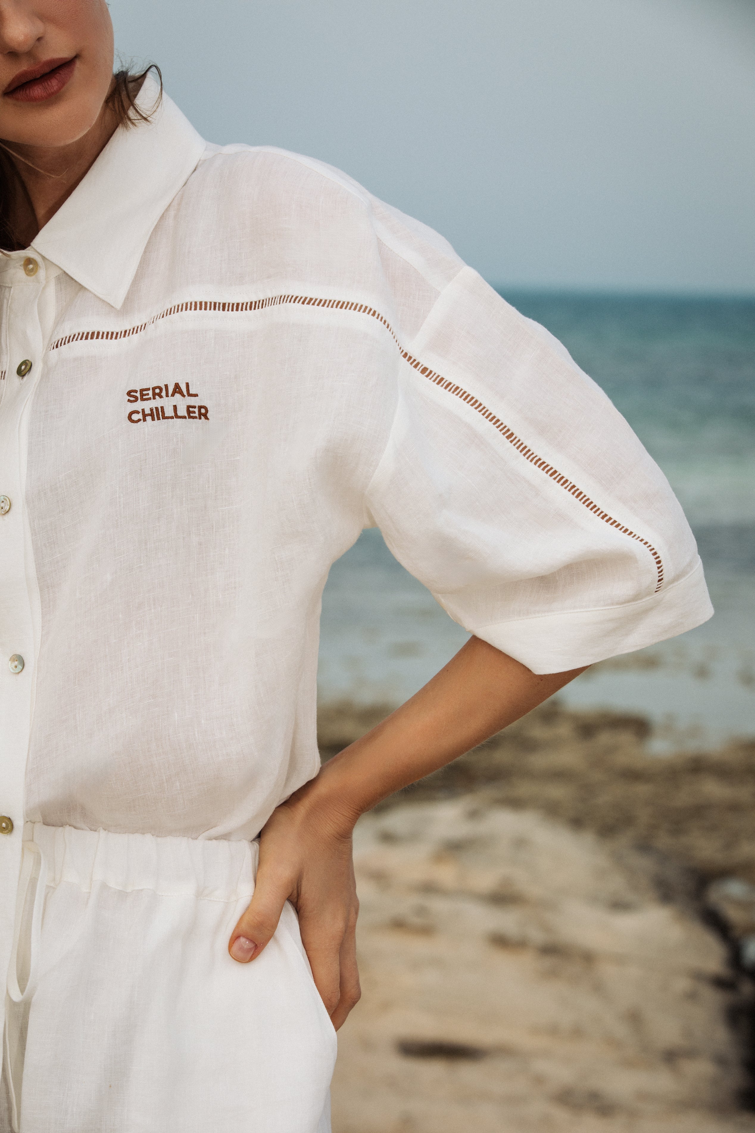 Model wearing Omni The Label’s white linen shirt and shorts set, standing in a minimal outdoor setting, embodying effortless summer style with a relaxed yet polished silhouette.UAE, KSA, Qatar