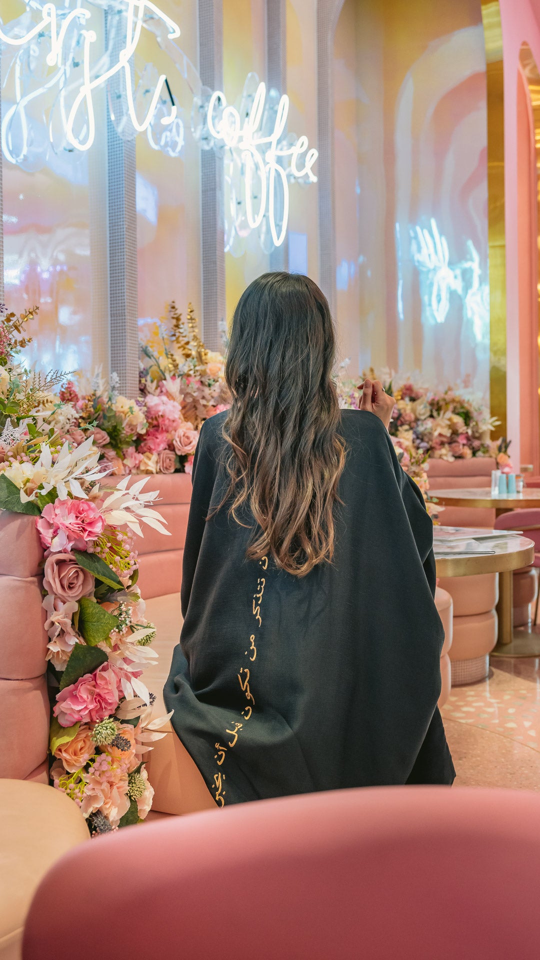 Back view black abaya with gold embroidery in floral cafe setting Omni The Label UAE Qatar KSA