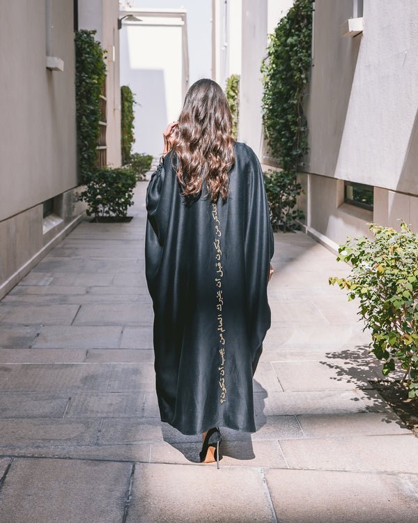 Outdoor back shot of black Abaya with classic sleeves with gold embroidery flowing silhouette Omni The Label UAE KSA Qatar