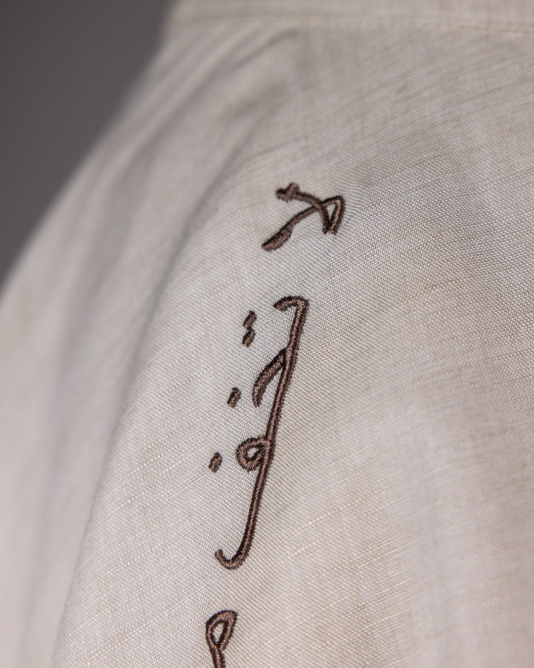 Close-up of Arabic embroidery on beige skirt, translating to 'Talk to me so I can see you.'
