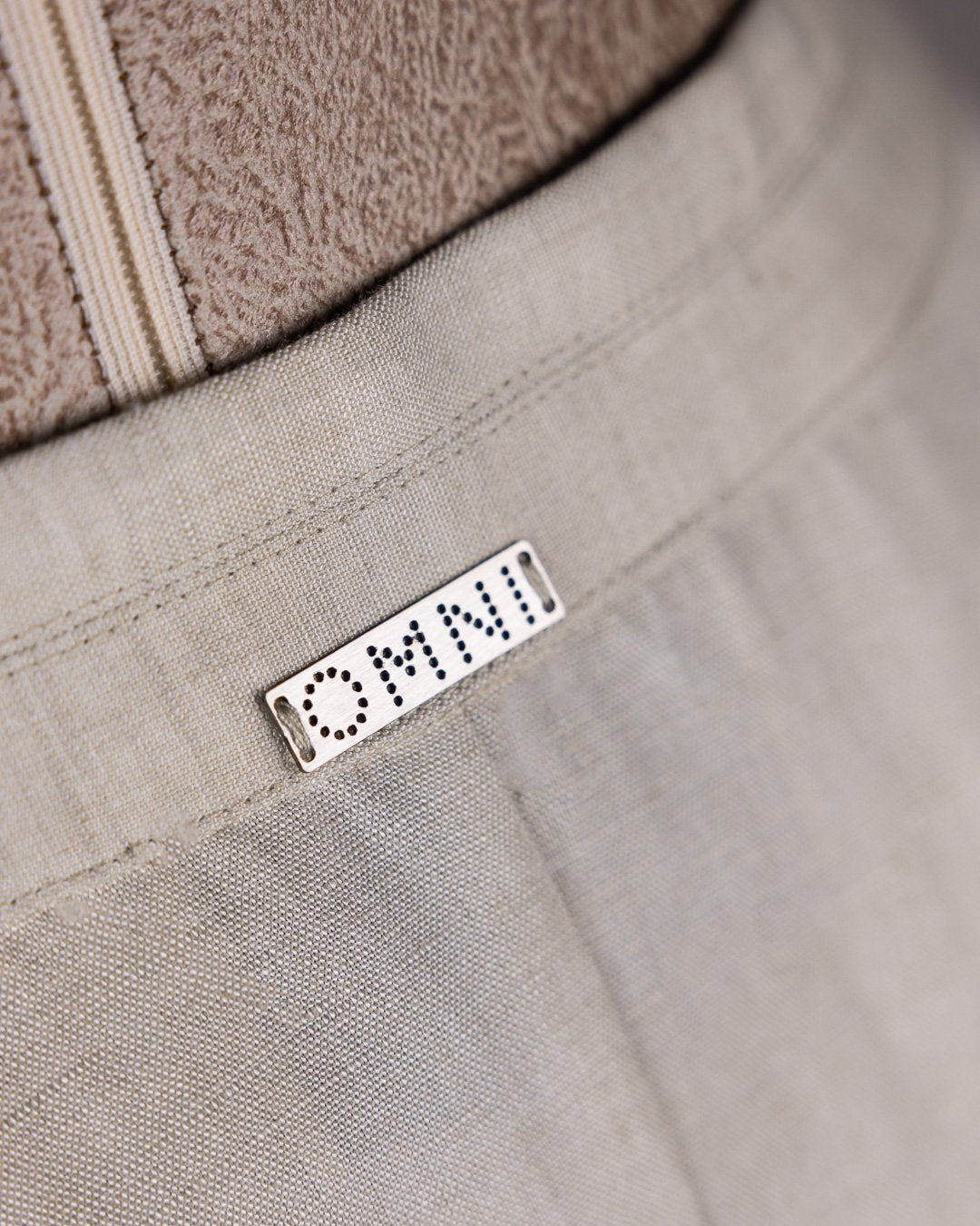 Close-up of Omni The Label’s signature metal tag on beige skirt. Qatar UAE KSA