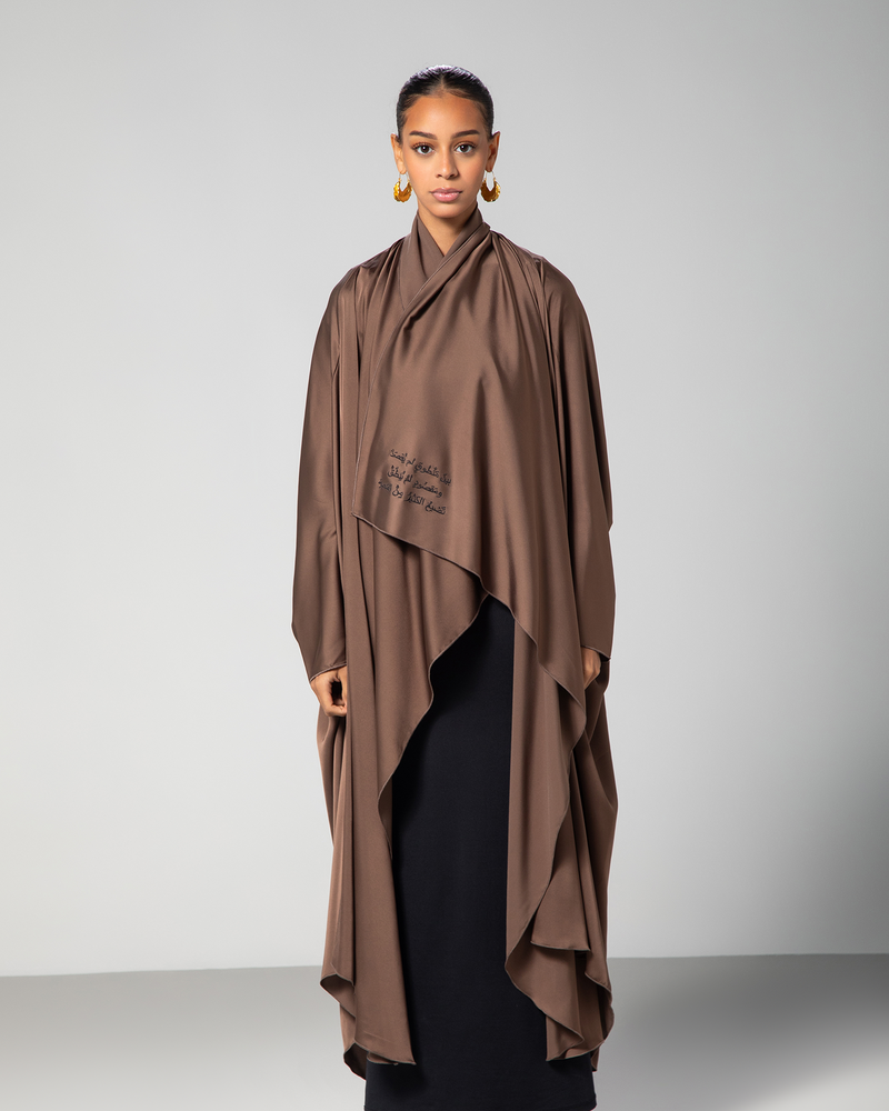 A model wearing a brown silky flow abaya with cascading layers and Arabic calligraphy embroidery on the front.