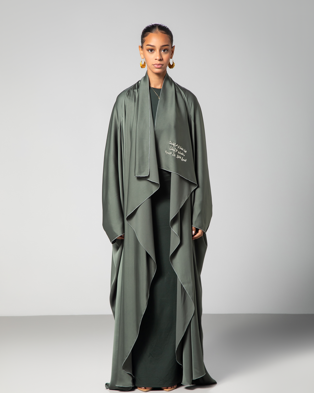 A woman wearing a green flowing abaya with cascading layers and embroidery on the front.UAE Qatar KSA