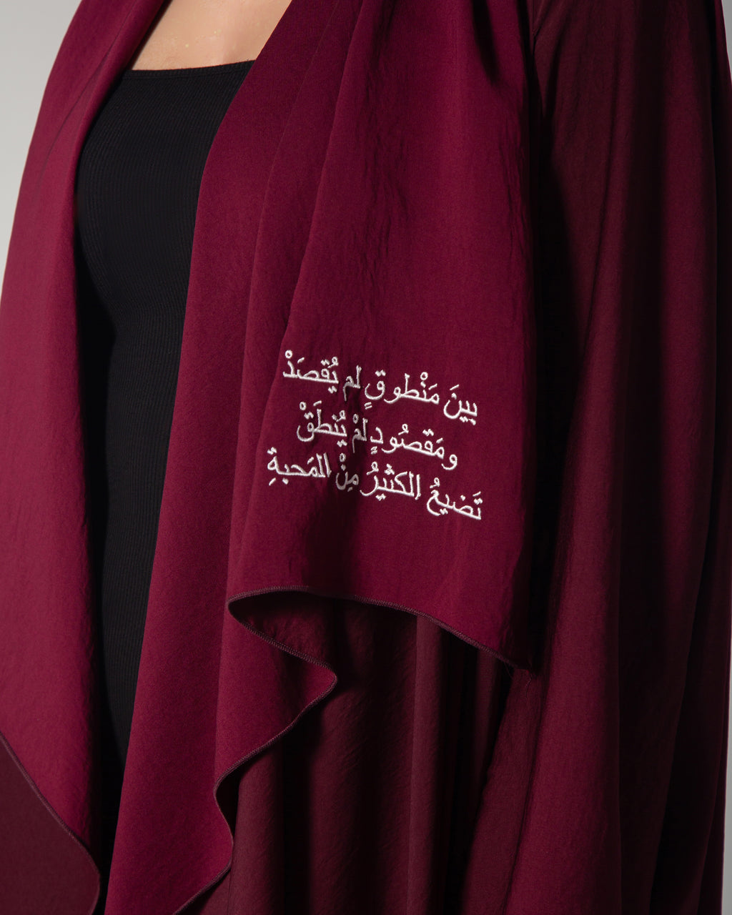 A woman wearing a burgundy abaya with a flowing design and Arabic calligraphy embroidery on the front, middle east saudi kuwait qatar modest fashion 