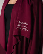 A woman wearing a burgundy abaya with a flowing design and Arabic calligraphy embroidery on the front, middle east saudi kuwait qatar modest fashion 