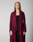 A woman wearing a burgundy abaya with a flowing design and Arabic calligraphy embroidery on the front. saudi qatar kuwait fashion omni the label 