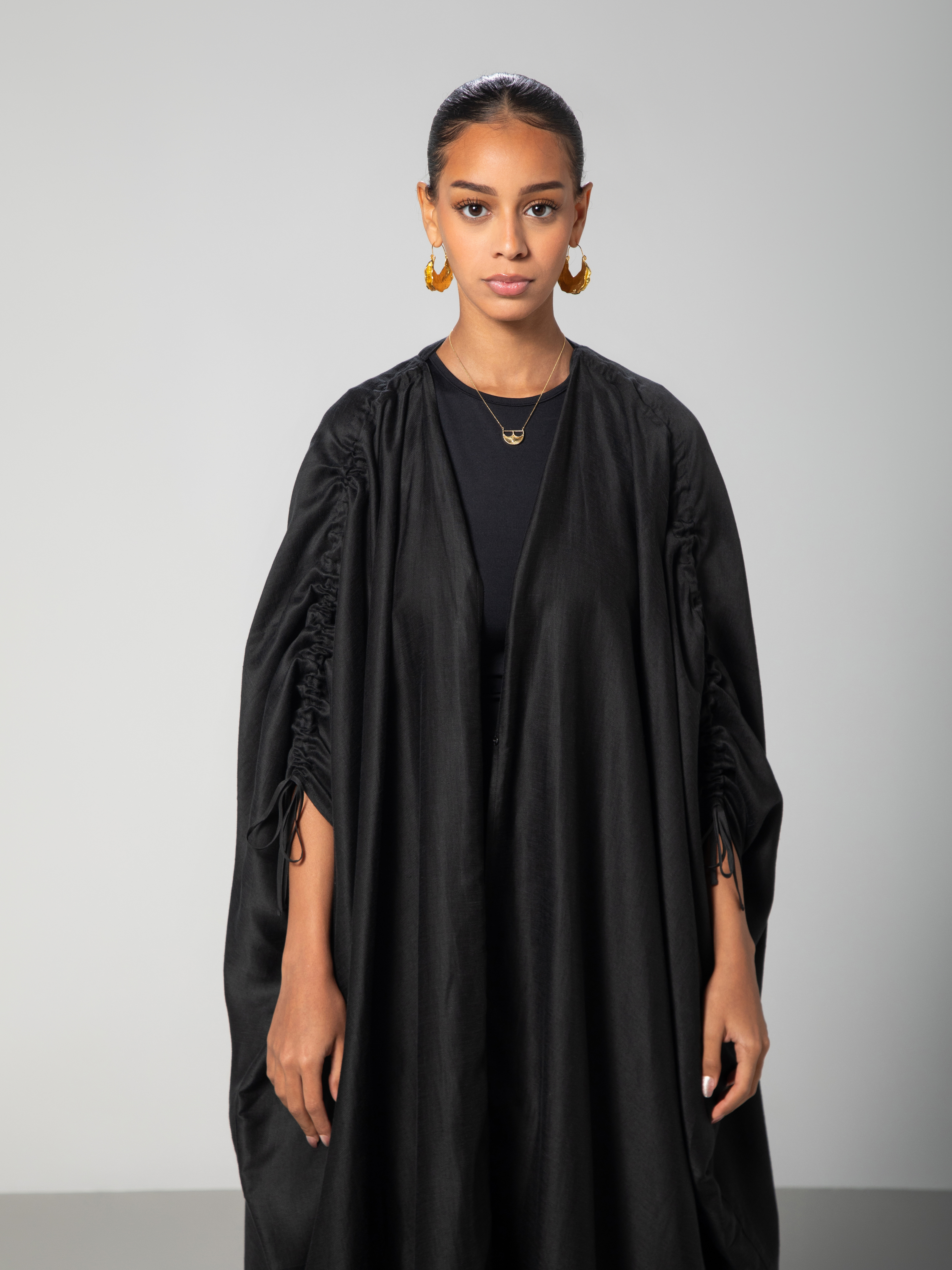 a black abaya with adjiustable sleeves with arabic caligraphy embroidered on the back by omni the label uae ksa qatar doha 