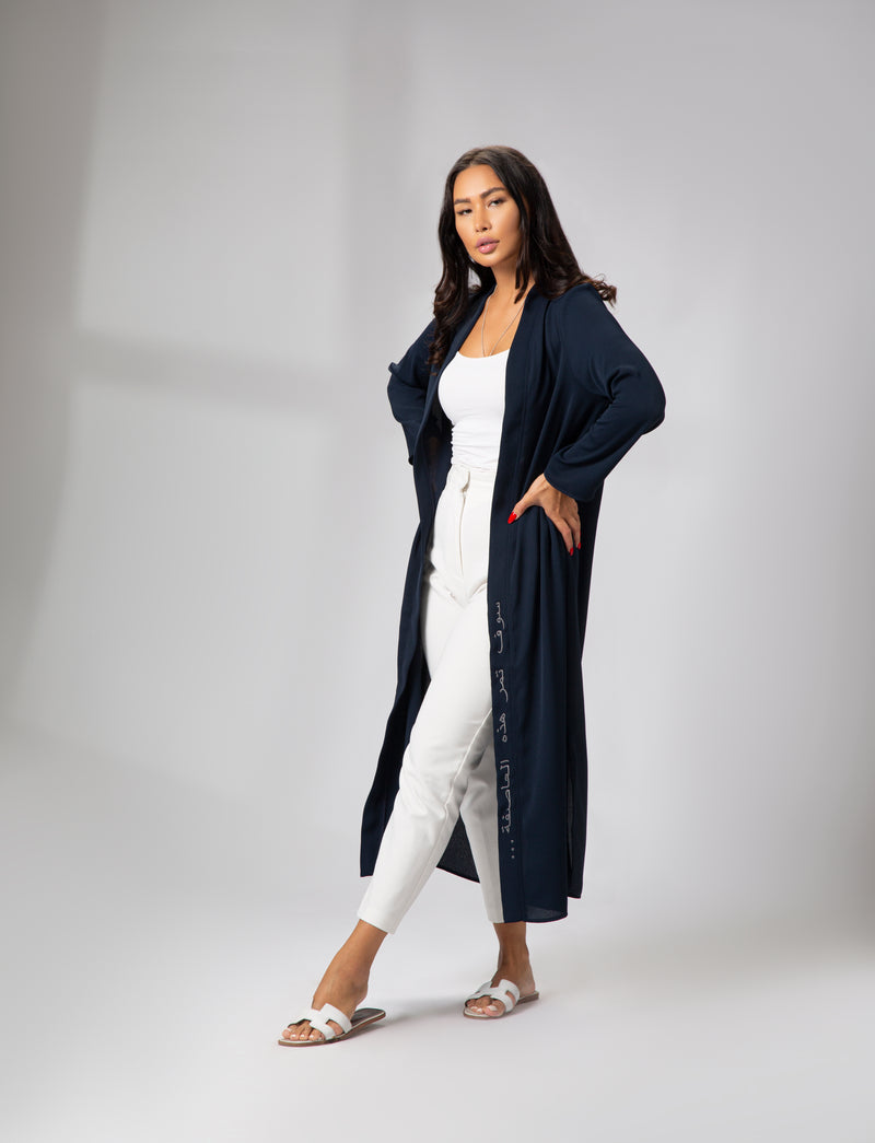 A woman modeling a navy blue long-sleeve kimono with delicate embroidery on the front left side, paired with a white top and white trousers KSA UAE Qatar
