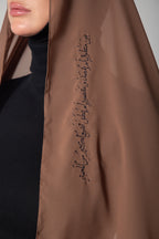 A woman wearing a brown scarf with black embroidery.