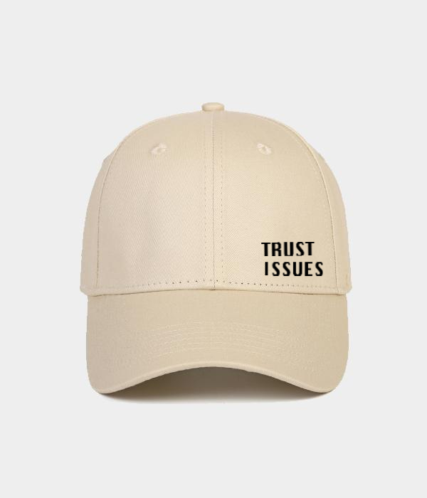 A beige baseball cap with 'TRUST ISSUES' printed in black text on the front.