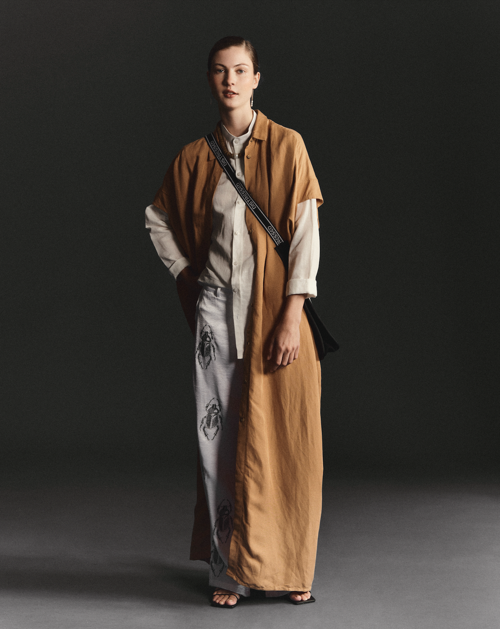 Model wearing camel brown embroidered cover-up by Omni The Label styled over printed white trousers studio shot Qatar UAE KSA