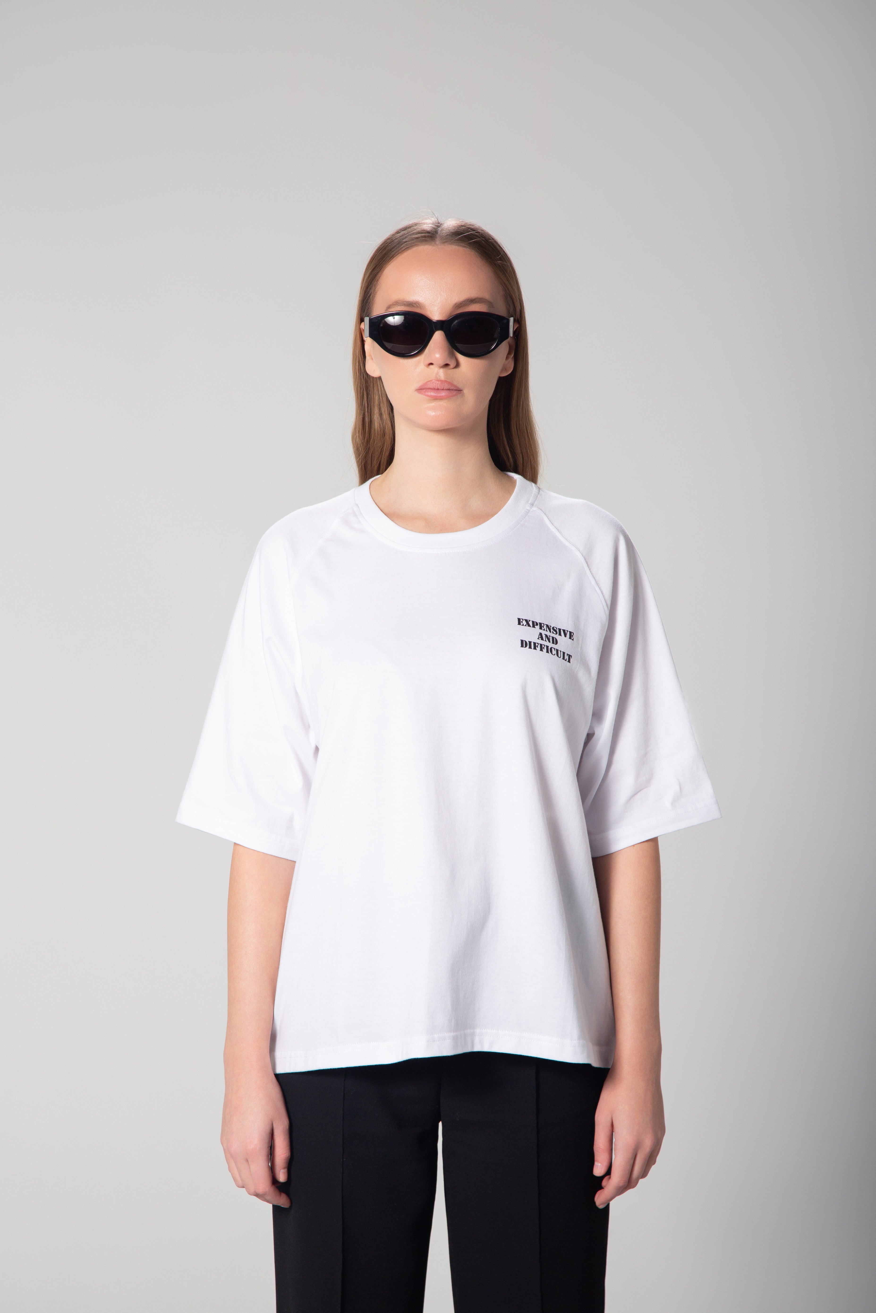  A white oversized t-shirt with the words Expensive and Difficult  printed in bold, contrasting lettering on the front. The relaxed fit and dropped shoulders give it a modern, effortless look. Perfect for casual and statement styling.